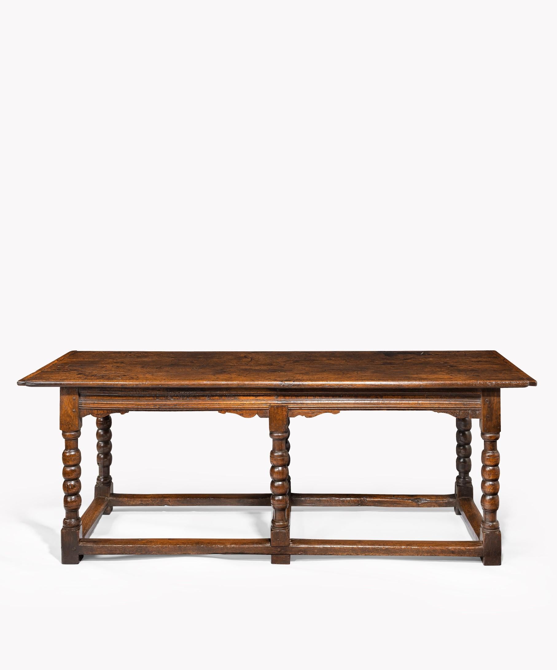 A late 17th century oak hall table; the table's well figured two plank top above a molded frieze in sized with the date 1699 above turned legs united by stretchers. This table retains a superb color and patination and would also make a superb
