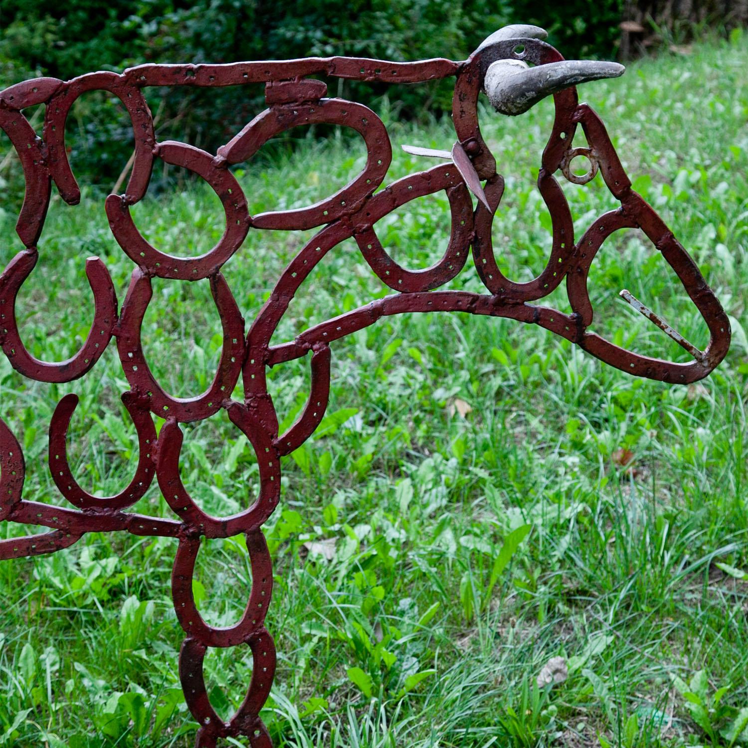 Sculpture of a cow with horns, made of single horseshoes, welded together. The horseshoes are painted red.