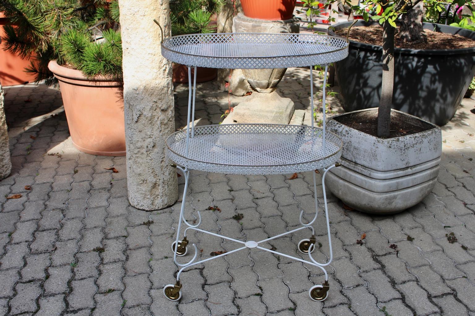 This extraordinary two-tiered bar cart consists of wire steel perforated sheet metal white lacquered, brass details and four white rubber wheels.
The lying on top tray is movable, maybe for serving drinks.
Another special feature of this bar cart