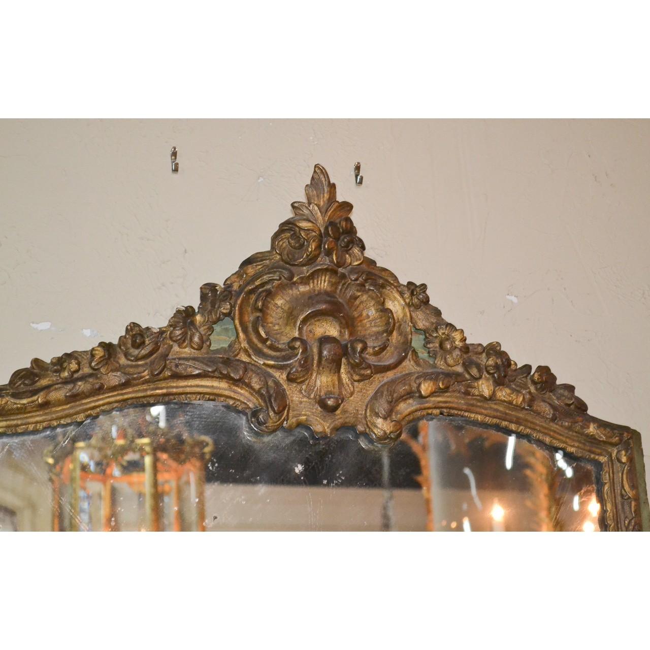 Splendid 18th century French Regence style parcel gilt wall or console mirror. The crest with finely carved leaf-sprays, shells, blossoms, and trailing flower vines. The inner border carved in relief and trimmed with a painted green-tint outer