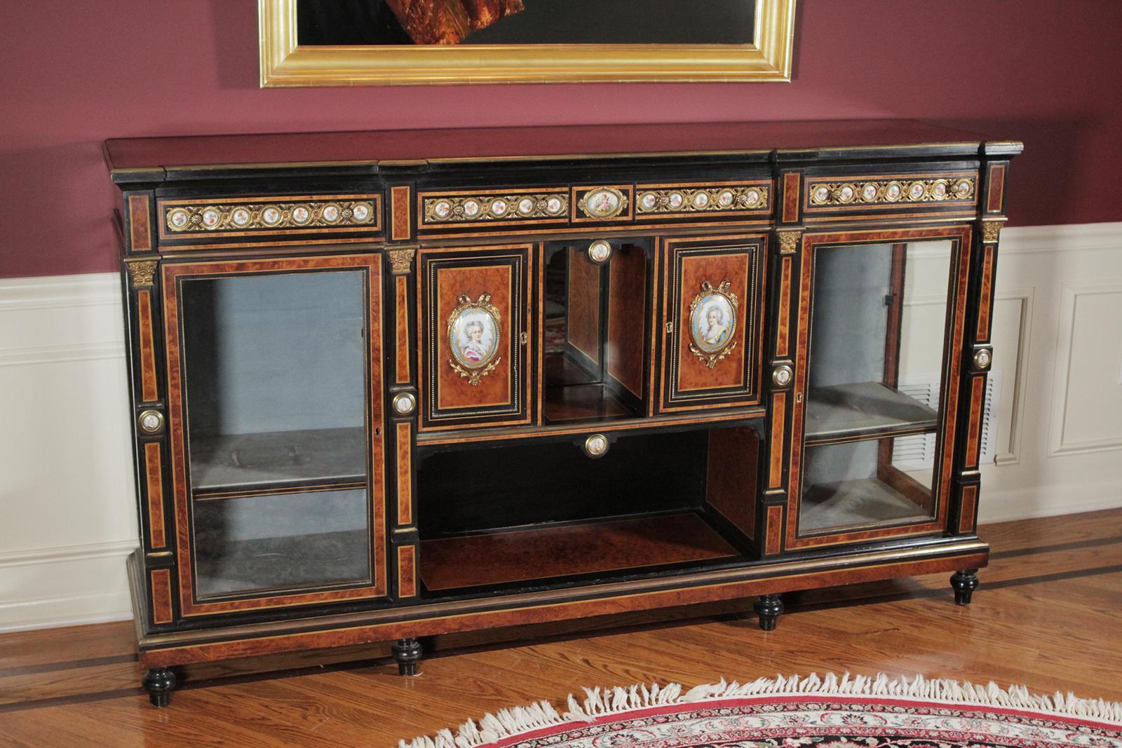 A burl walnut and ebony credenza sideboard with bronze and porcelain mounts. The burl walnut framed in ebony with ormolu mounts and hand-painted porcelain plaques on the doors and aprons. The front with two glazed doors on each side with open and
