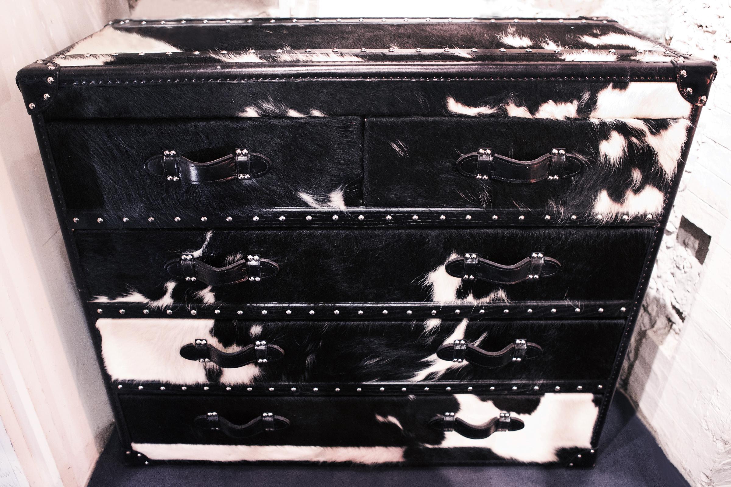 Wild black and white cowhide high chest
with structure in solid wood and covered with 
natural black and white cowhide. With black
genuine leather handles and with polished 
stainless steel nails. With five drawers with black 
fabric inside.