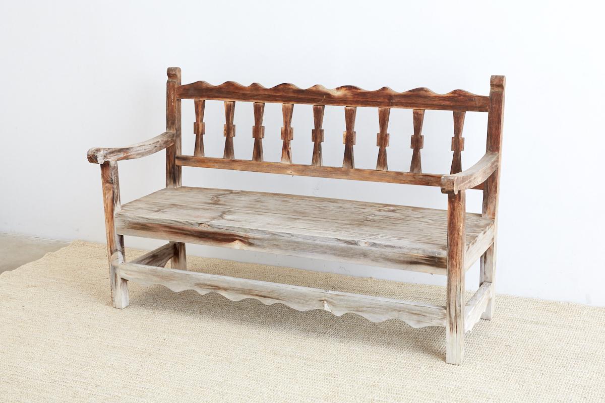 Rustic pine bench made in the California Rancho Monterey style with a beautiful distressed and faded patina. Excellent joinery with an open slat back style and a flat seat. The natural wood has faded from exposure but still has some interesting warm