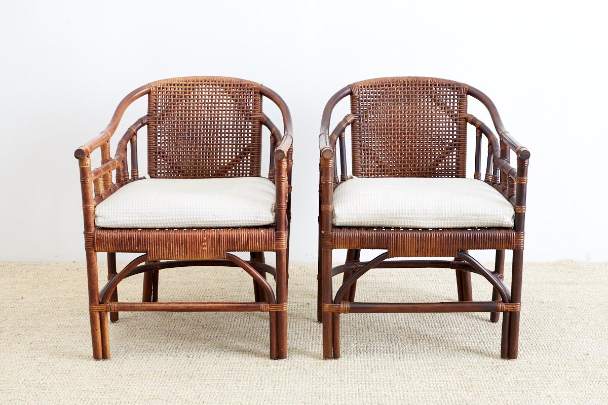 Stylish pair of bamboo rattan barrel back lounge chairs made in the manner of McGuire. Featuring a bent rattan frame with a woven seat and back. The chairs are supported by a six leg design with decorative stretchers and bamboo strapping. Each has a