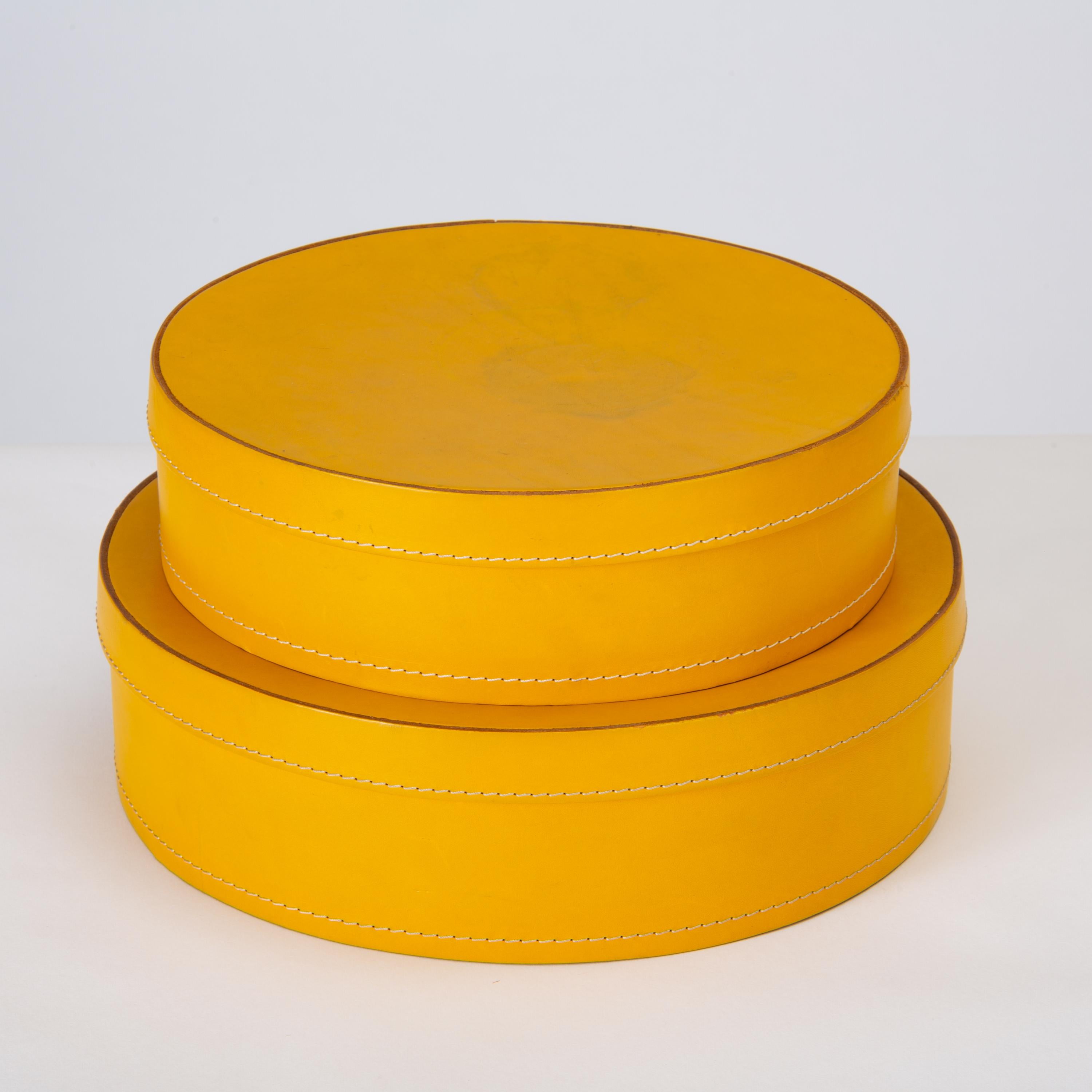 A pair of round nesting boxes in mustard-colored leather by Italian company Arte Cuoio e Triangolo. The “1980” design features a rounded frame, straight sides, and a snug-fitting lid with contrast stitching in Danish flower thread. This set has two