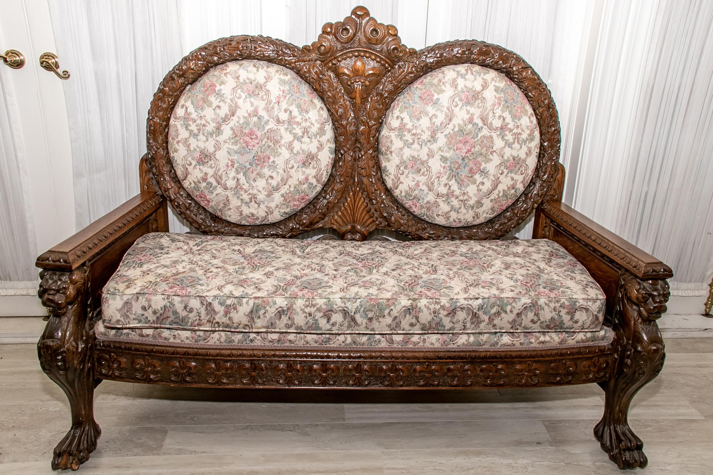 Late 19th century carved settee, oak, double balloon back with scrolled foliate carved motif and central fleur-de-lis crest, scrolled floral upholstered inset backs and long seated cushion, fleur-de-lis relief carvings along skirt flanked with two