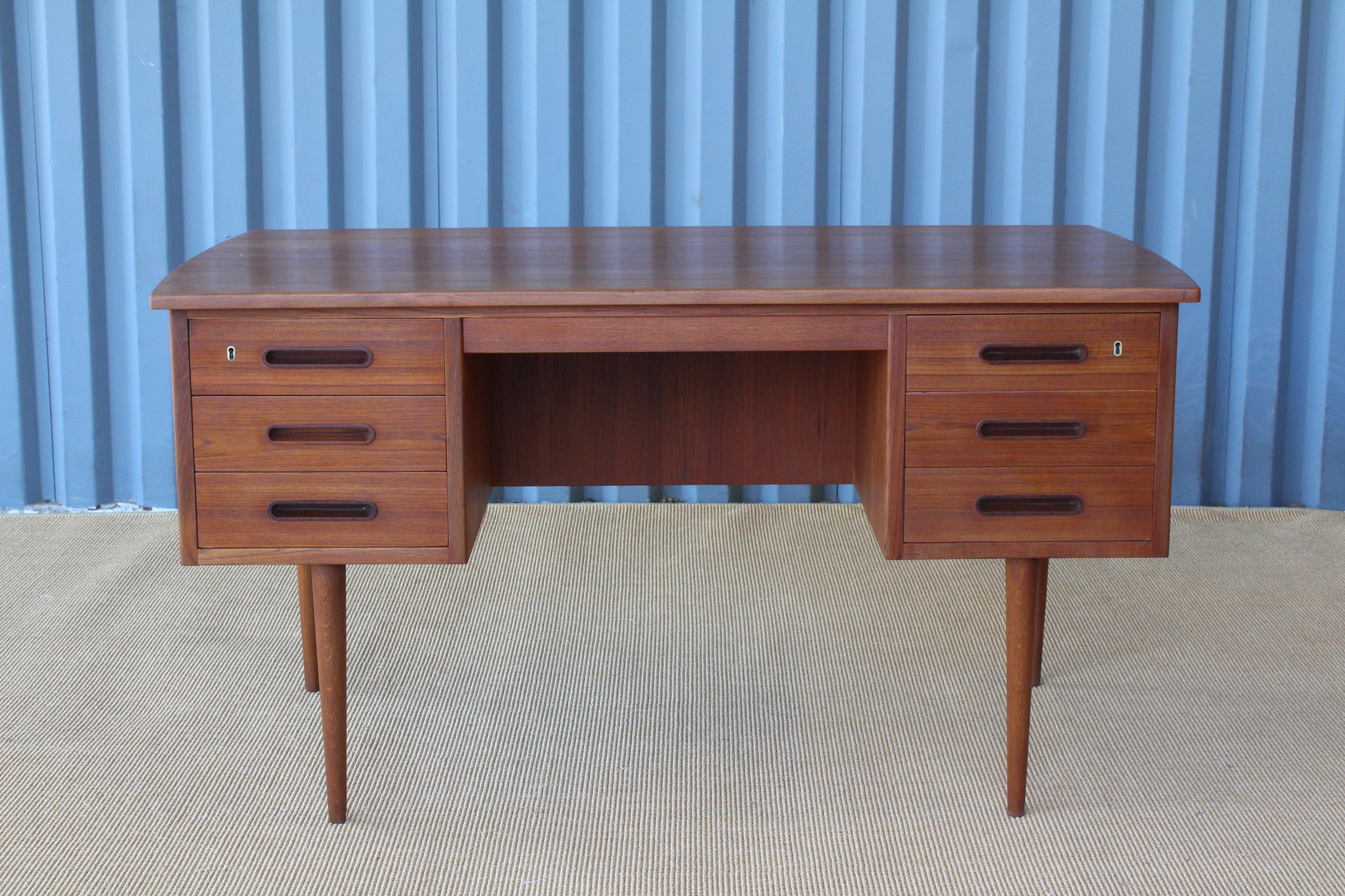 1950s Danish teak desk. The front side is slightly curved, backside features a bookshelf. Total of six dovetail drawers with two locking top drawers. Includes original key. Newly refinished.