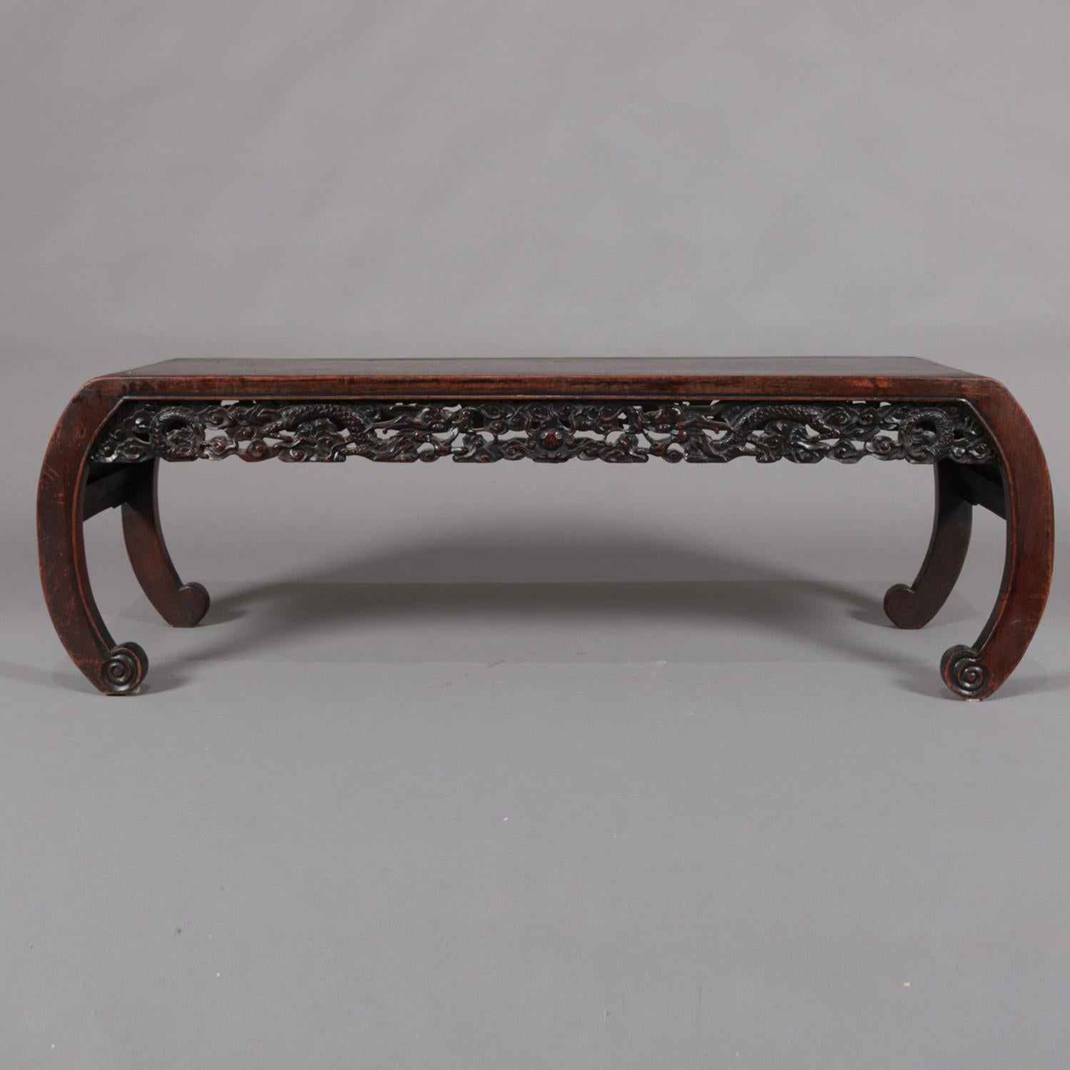 Antique Chinese figural low table features hardwood construction with rectangular top over carved and pierced apron having dragon and foliate design, raised on scroll form legs with paneled sides and scrolled horse hoof feet, 20th