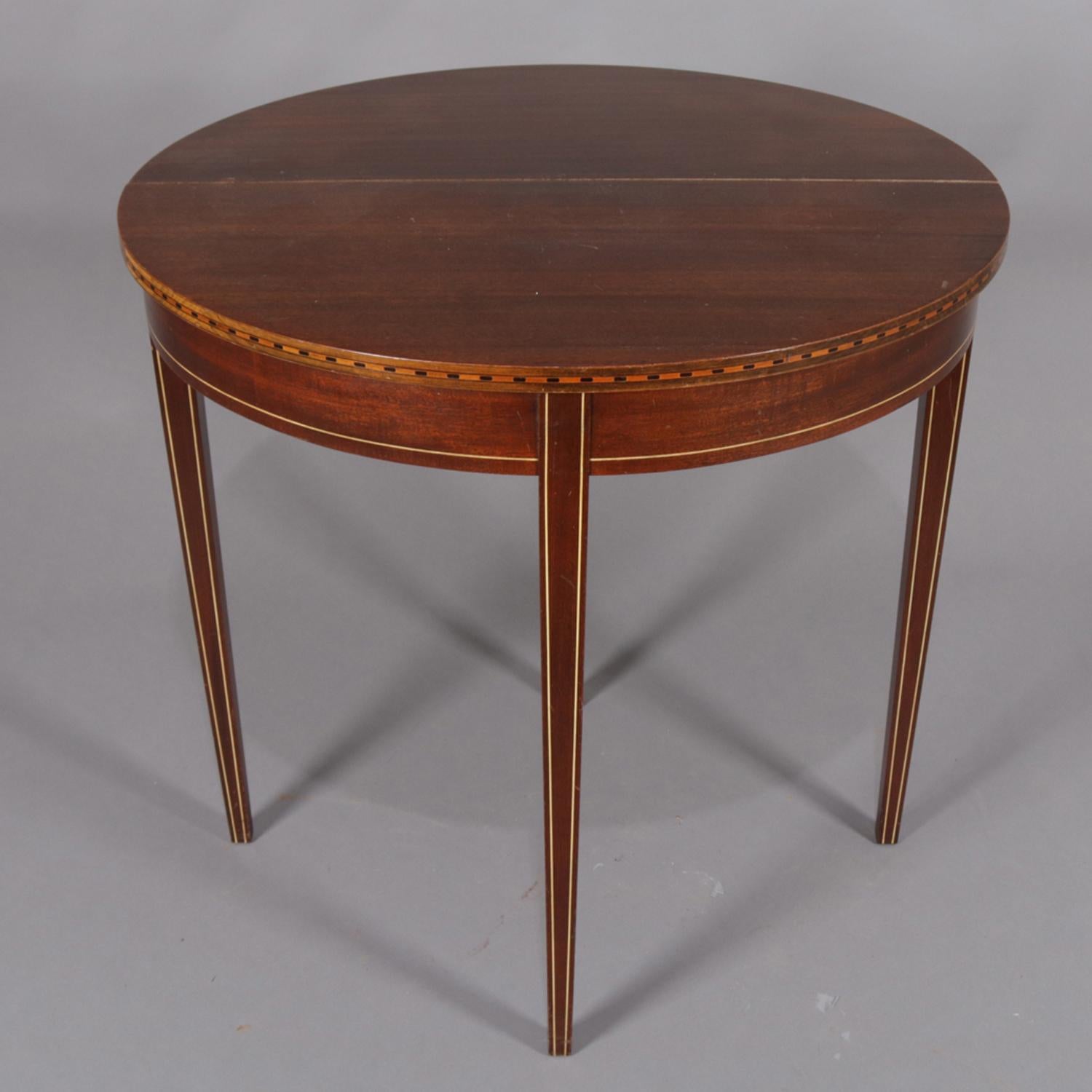 Antique Hepplewhite style game table by Brandt Furniture Co., Maryland features mahogany construction in demilune form when closed and round when open having edge marquetry banding in satinwood and ebonized block pattern and raised on square and
