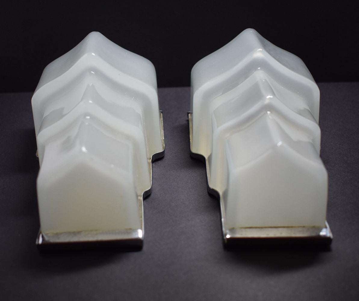 A golden opportunity to buy a wonderful pair of original 1930s Art Deco wall lights originating from England. Stepped in shape with a chrome back plate and surround which holds the opaque glass shades. The glass as a slight opalescent quality to it