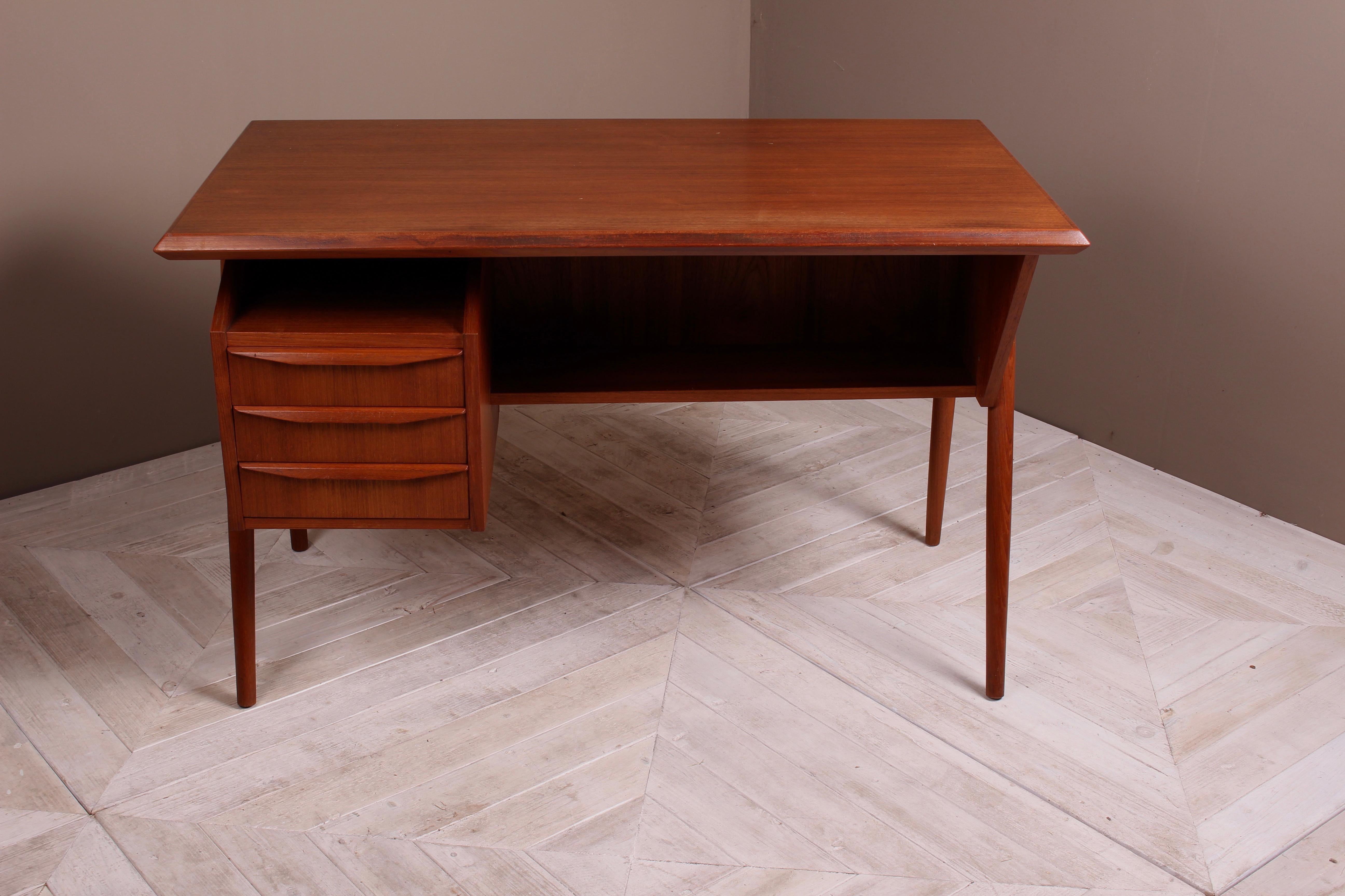 A classic midcentury Danish teak desk and chair by Gunnar Nielsen Tibergaard. The bevelled edge desktop above two lower shelf sections and three drawers. Large bookshelf to the rear. Standing on turned circular angled legs. In good condition for