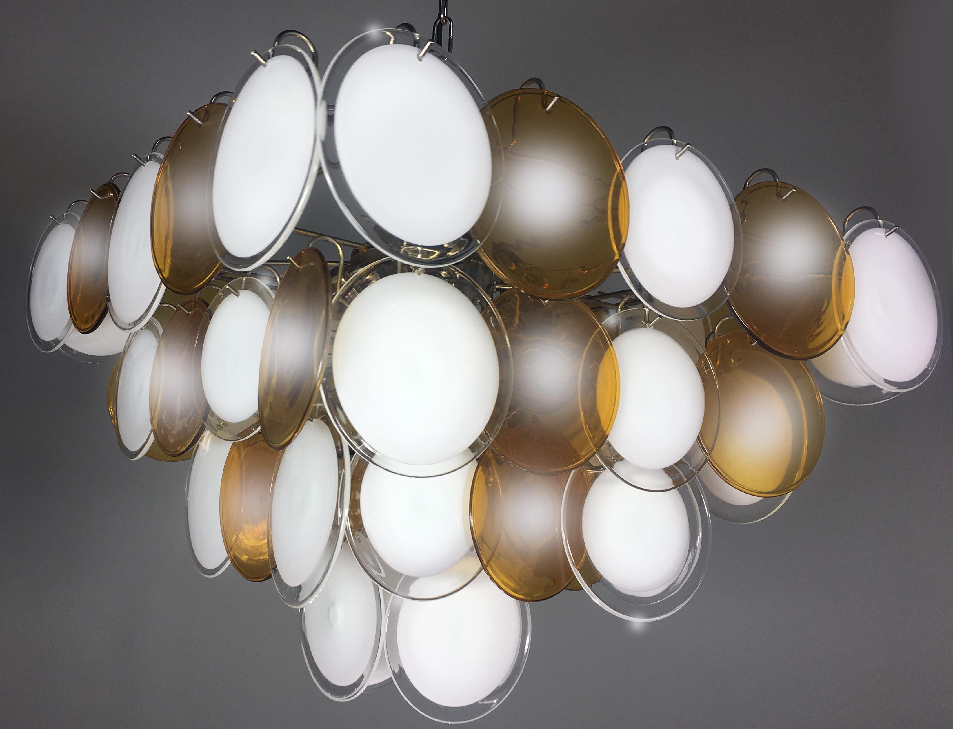 Each chandelier is made of 52 white and amber discs of precious Murano glass are arranged on four levels. Nine lights.