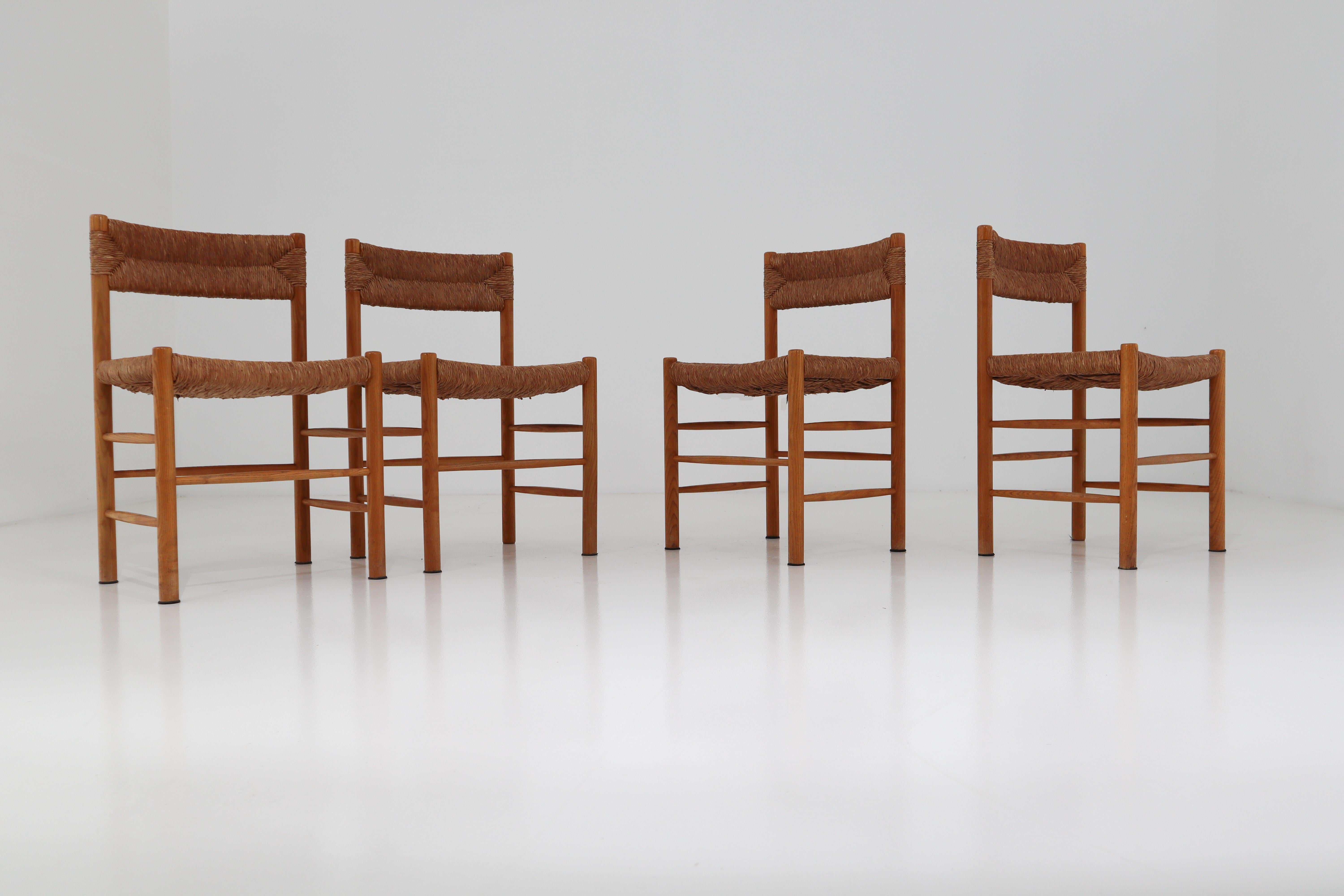 A pair of four dining chairs of wood and straw in one of the quintessential midcentury designs of their creator, the famous French furniture maker Charlotte Perriand. The four chairs are identical in the patina as in their very uniform state. These