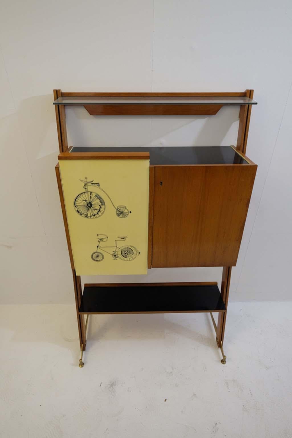 Midcentury Italian bar with original Fornasetti style bicycle printed yellow formica panels on the front.
The body of the cabinet is made in oakwood, with yellow formica lining on the interior as well as a black formica plate on the inside of a