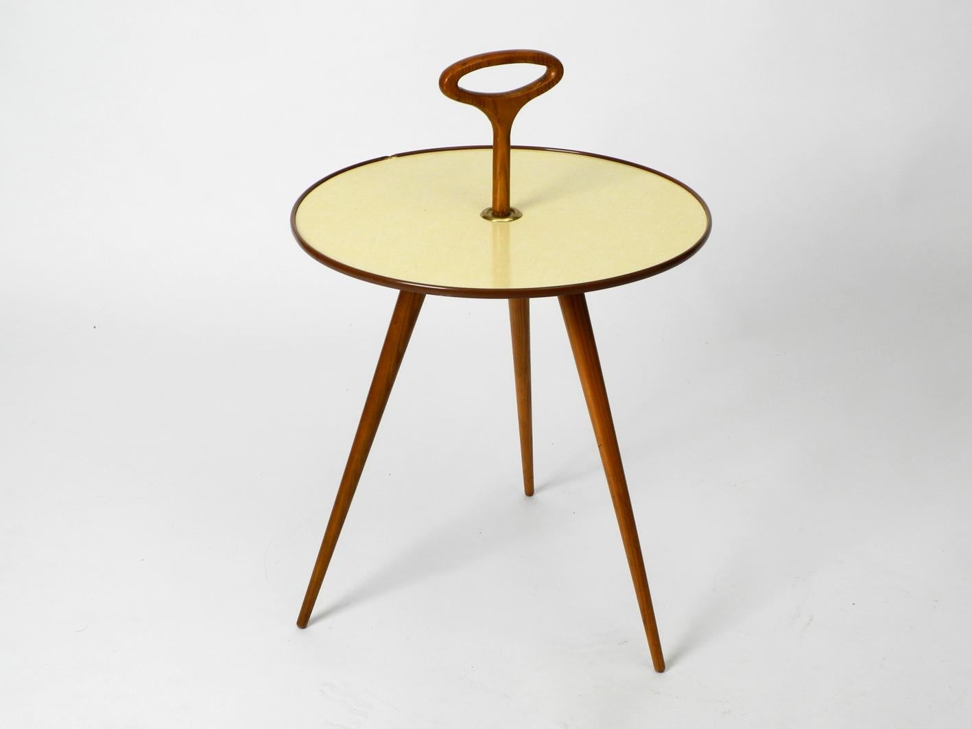 Very rare Mid-Century Modern round tripod table with handle top. Made in Germany. Beautiful very unusual design in original condition. Round beige plate covered with formica.
Frame is made of clear lacquered walnut.
Very good condition, there is