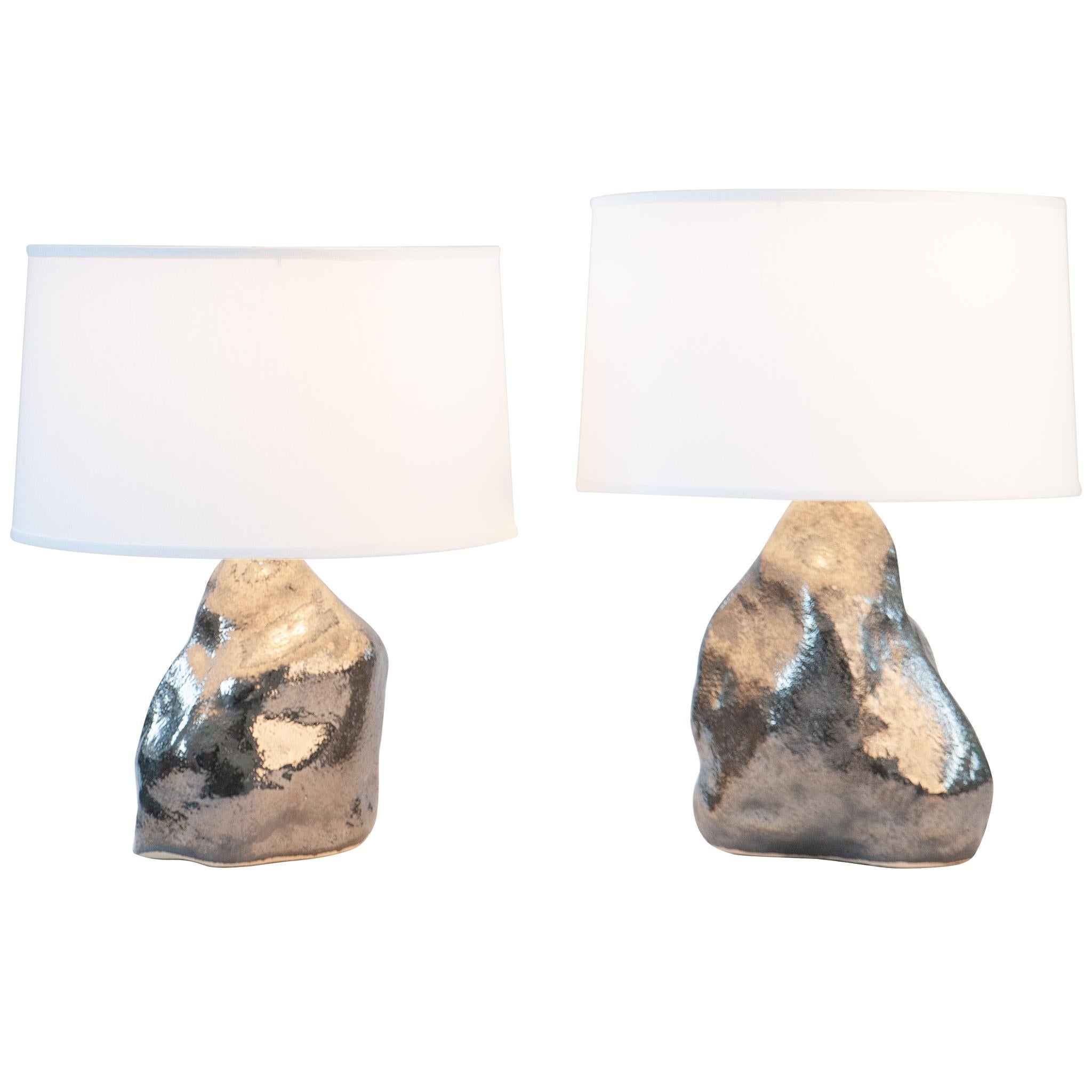 The platinum Amorphous table lamp pair ground and illuminate a room. Hand-sculpted from textured stoneware clay and fired with a lustrous platinum finish. Hand sculpted stoneware lamp bases, white linen textured fabric shades, fully dimmable 250