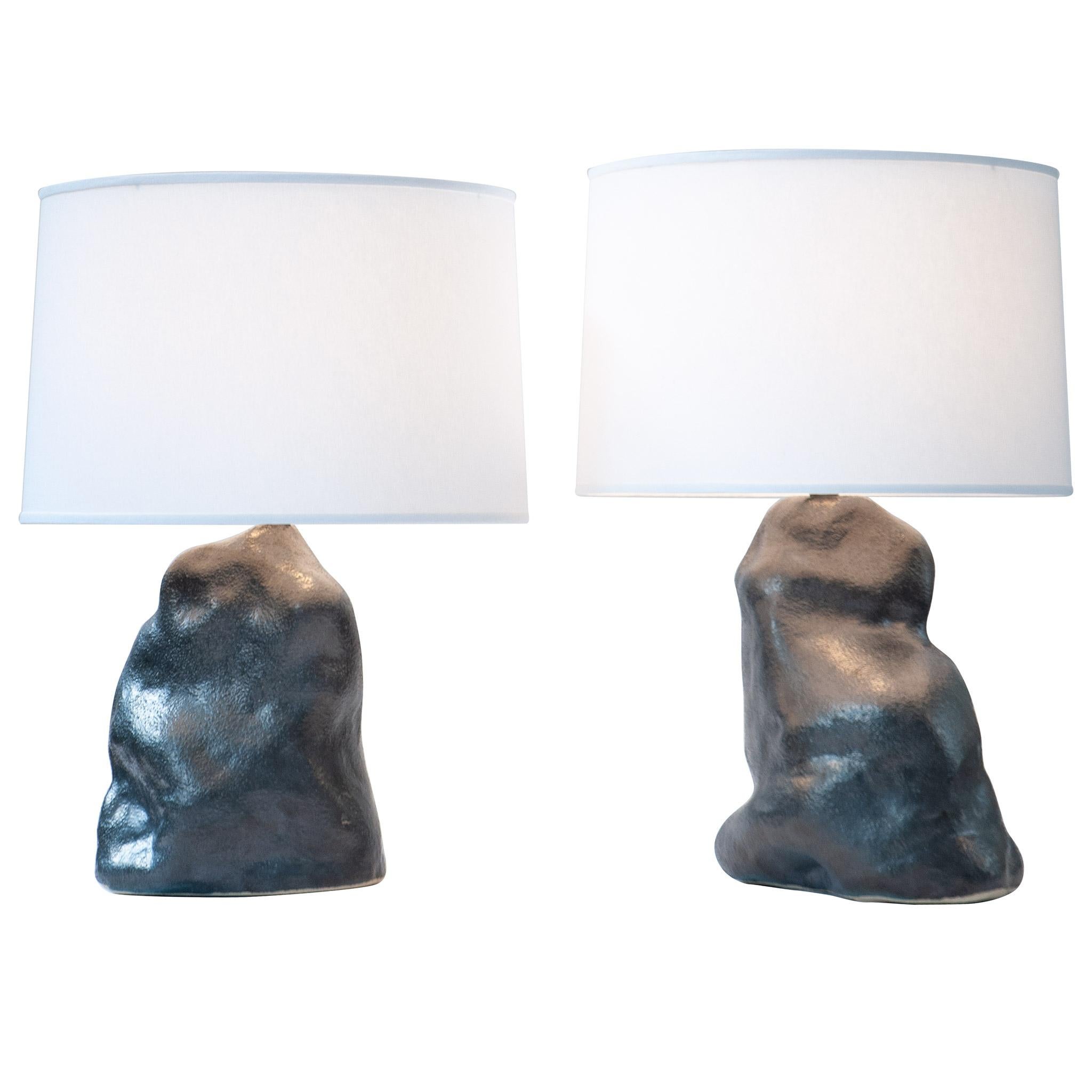 The metallic black amorphous table lamp pair ground and illuminate a room. Hand-sculpted from textured stoneware clay and fired with a lustrous metallic black finish. hand-sculpted stoneware lamp bases, white linen textured fabric shades, fully