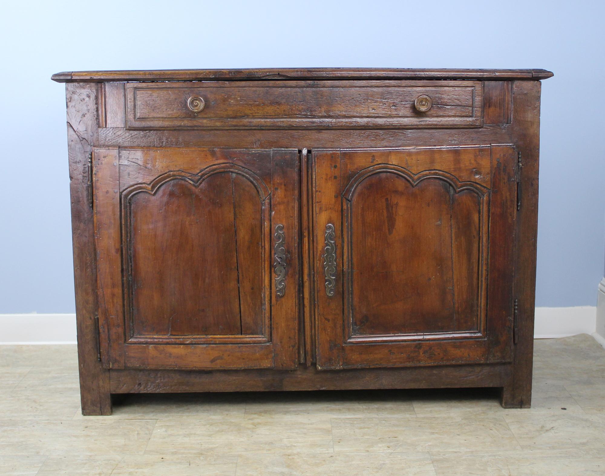 A handsome rustic country chestnut buffet with a single roomy drawer at the top. The two-doors close well and have charming carved inset panels. The interior shelf is no adjustable. Color and patina on this piece are excellent. Moderate distress