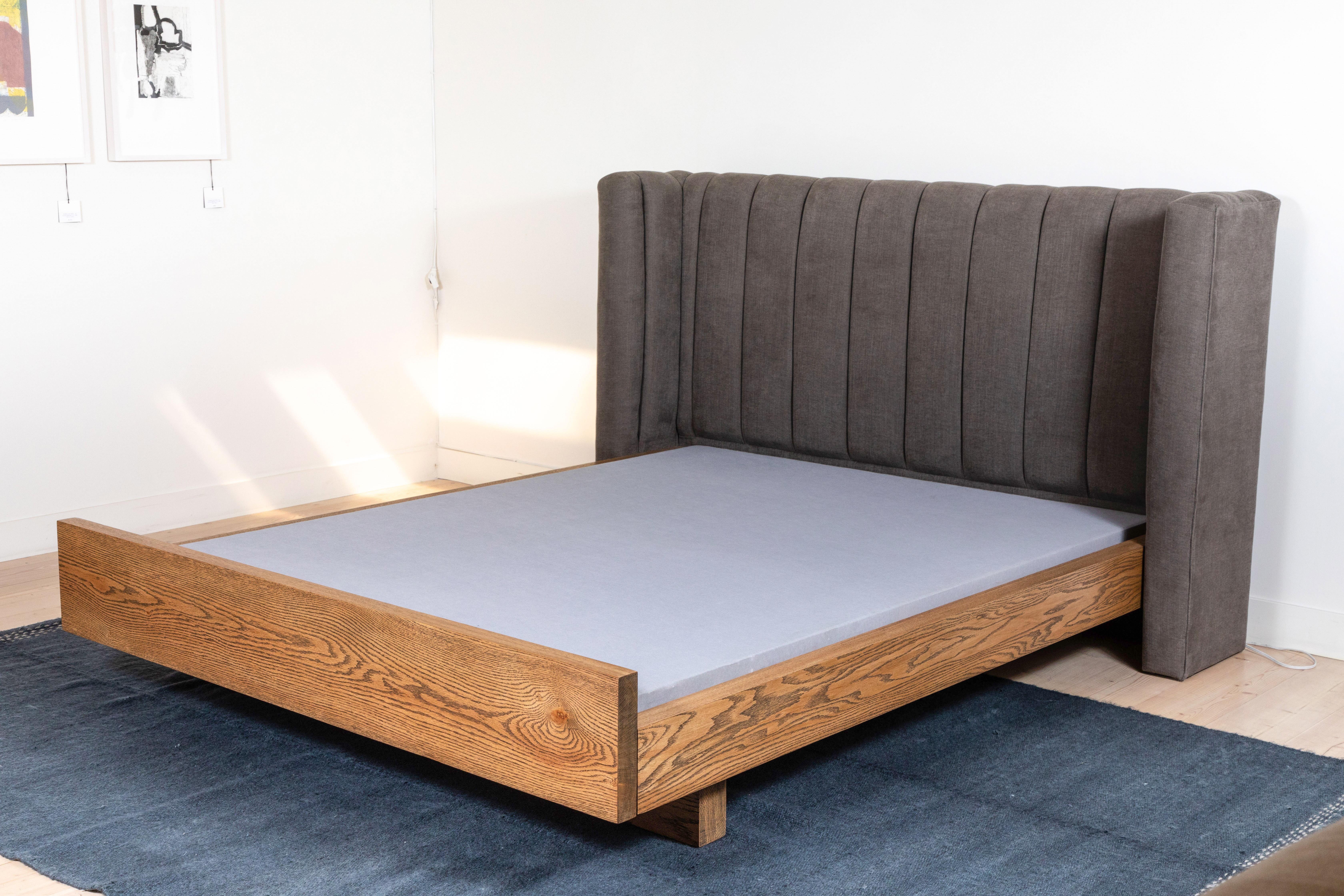 The Isherwood bed features a plinth base made of American walnut or white oak and a channel tufted shelter headboard. Slats are provided. Shown here as Queen-size in smoked oak. 

Available to order in Customer's Own Material with a 10-12 week lead