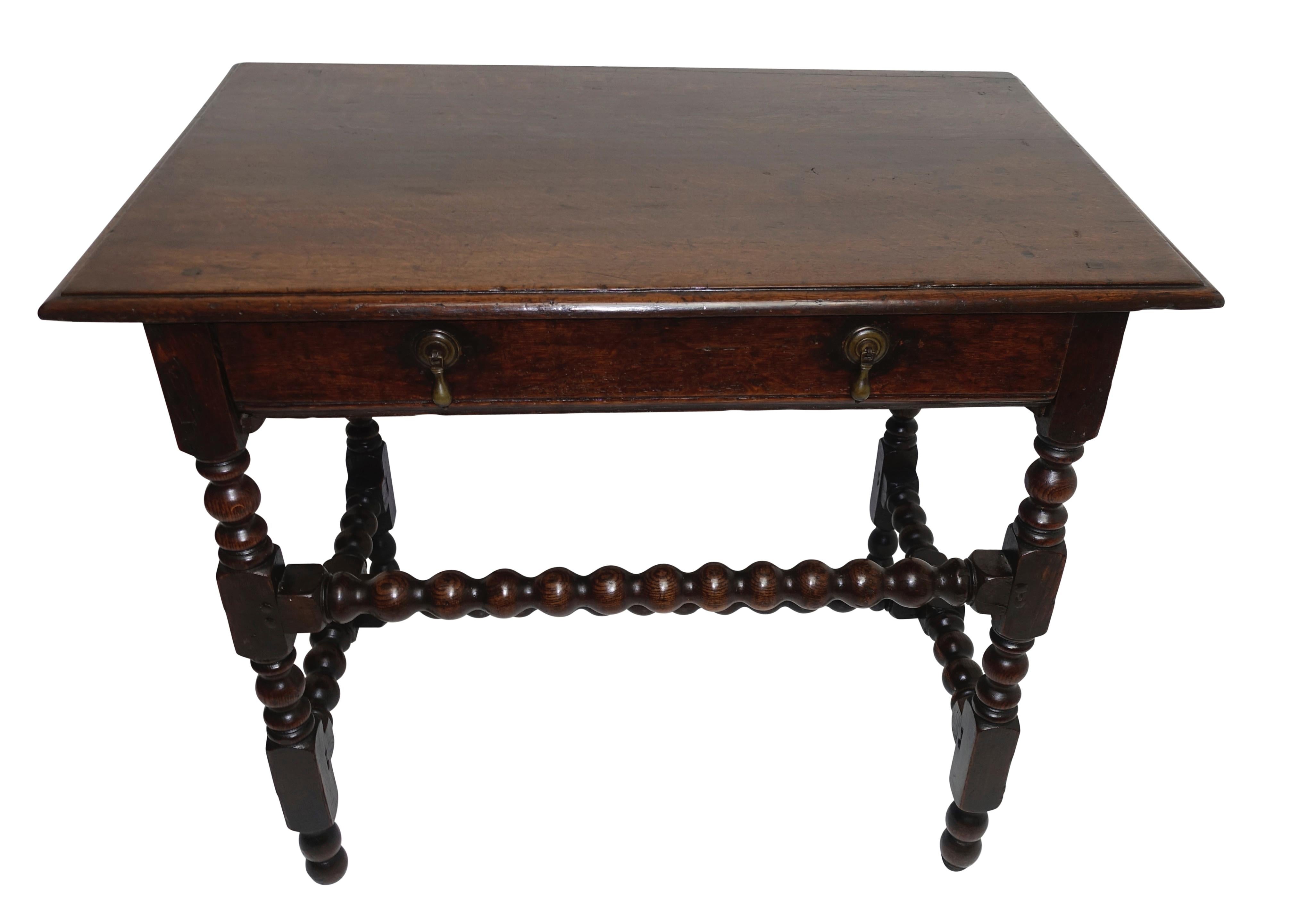 Oak side table or writing desk with a single drawer, having hand-carved turned legs and spool turned stretcher bars and with original hardware. England, late 17th to early 18th century.
