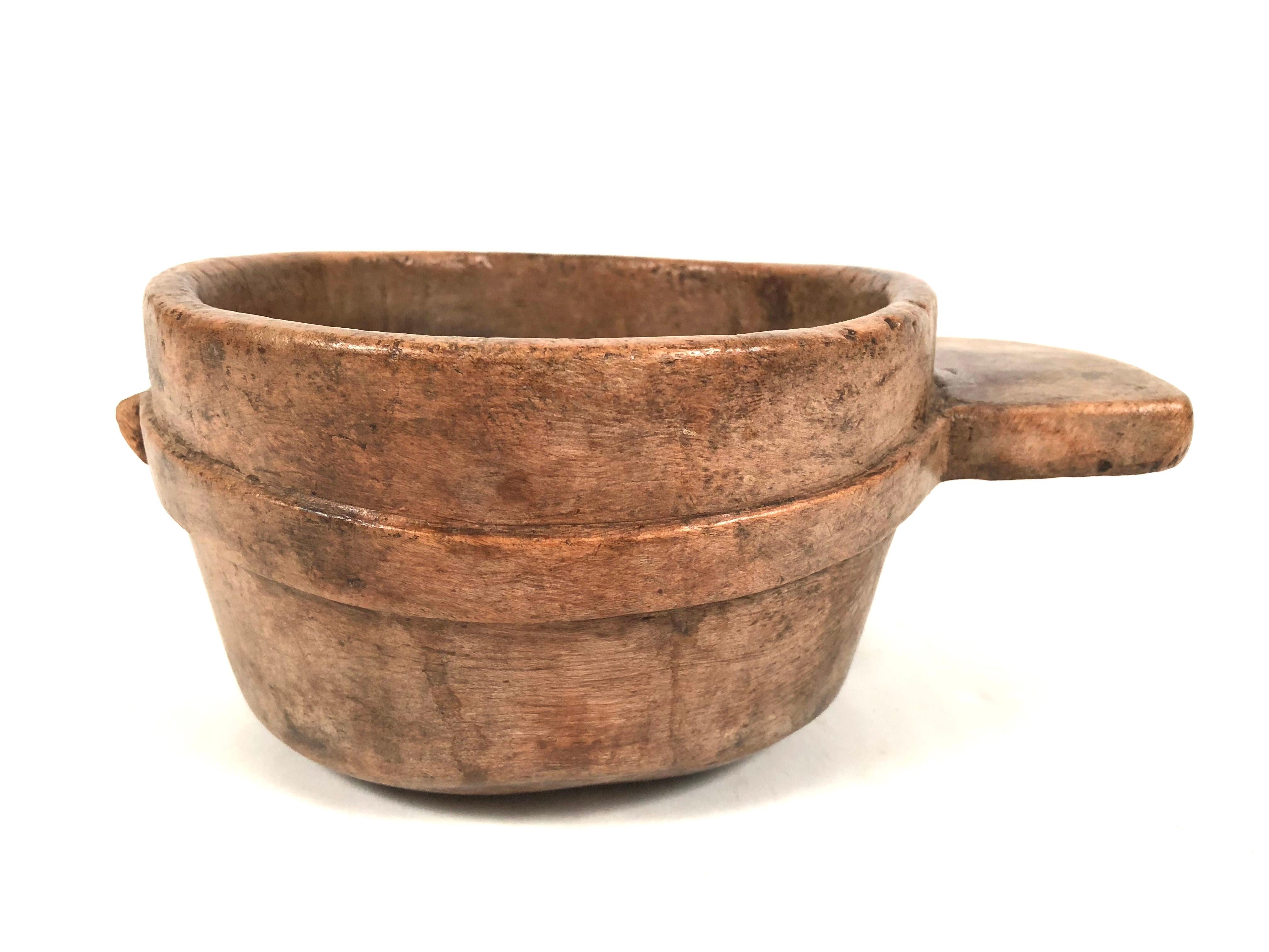 A sculptural and functional early primitive carved bowl, shaped like a porringer, with wonderful patina, of circular form with a shaped handle on one side and a raised carved band around the middle of the exterior and a raised knob on one side. Full