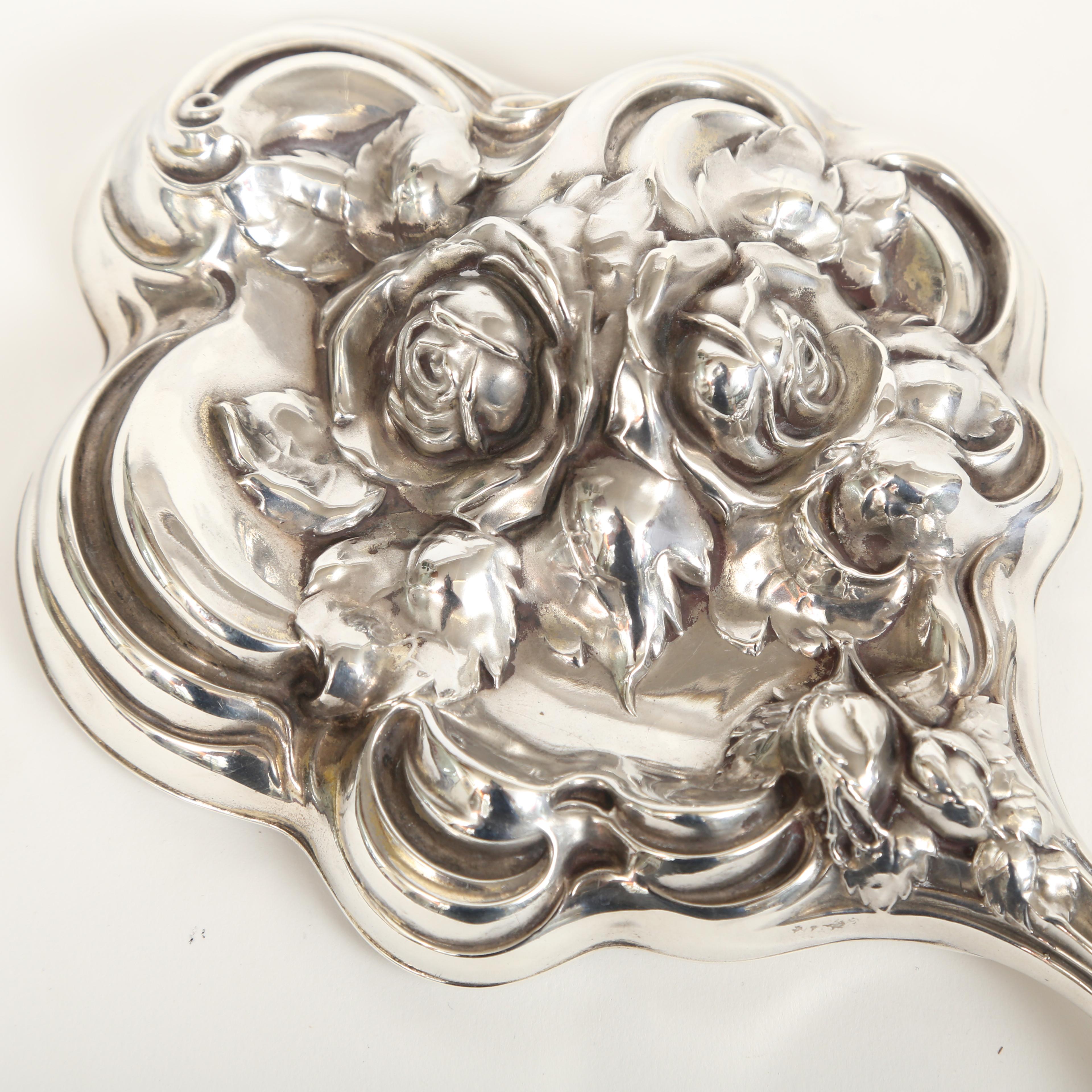 Shiebler Art Nouveau sterling hand mirror in the rose pattern. The repoussé work is in high relief. The mirror is beveled and cut to the shape of the mirror. There are some minor dents in the handle on the underside and a small scratch on the glass.