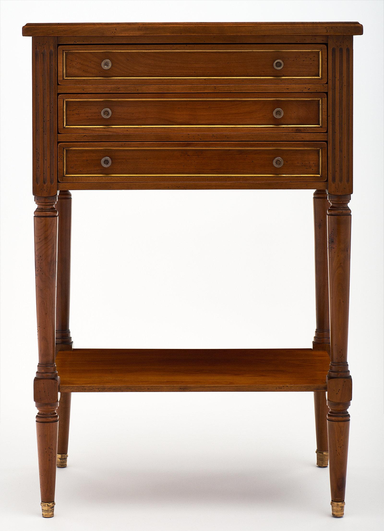 A refined Louis XVI style side table featuring three dovetailed drawers and a bottom shelf. This elegant piece is made of cheerywood and has a warm tone to the wood. Original hardware and brass capped feet!