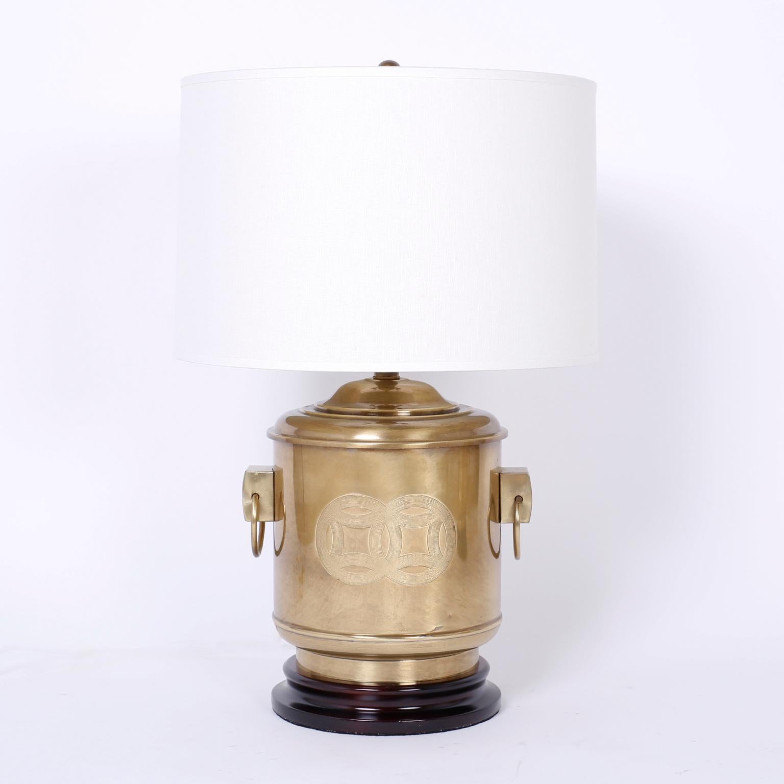 Chic pair of midcentury Chinese style brass table lamps with a canister form having overlapping circular good luck symbols, ring handles and turned wood bases.