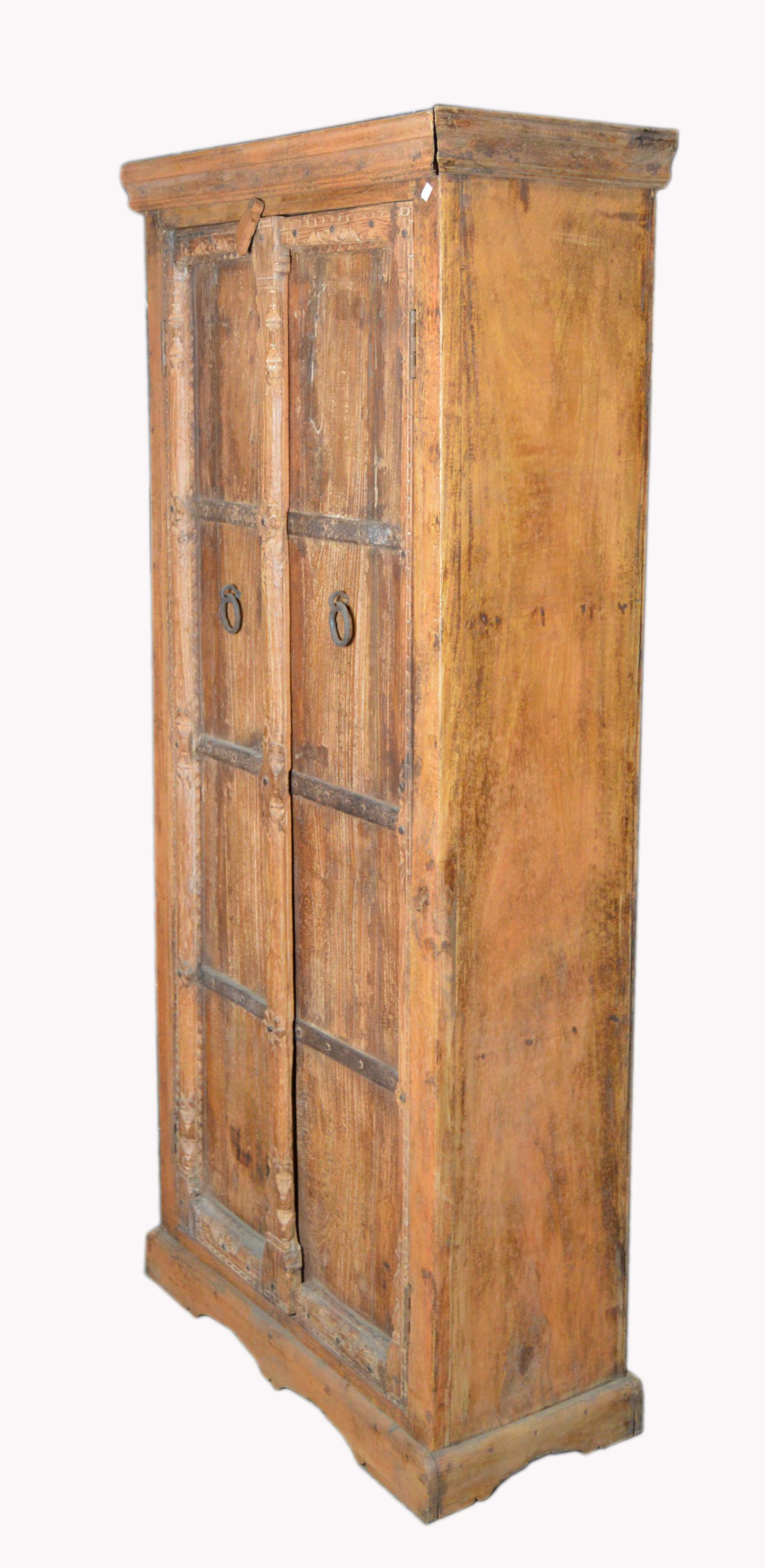 An vintage Indian wooden armoire with metal braces and brass handles. Born in India during the late-20th century, this wooden armoire features a molded cornice sitting above two elegant doors. Each door is accented with horizontal metal braces that