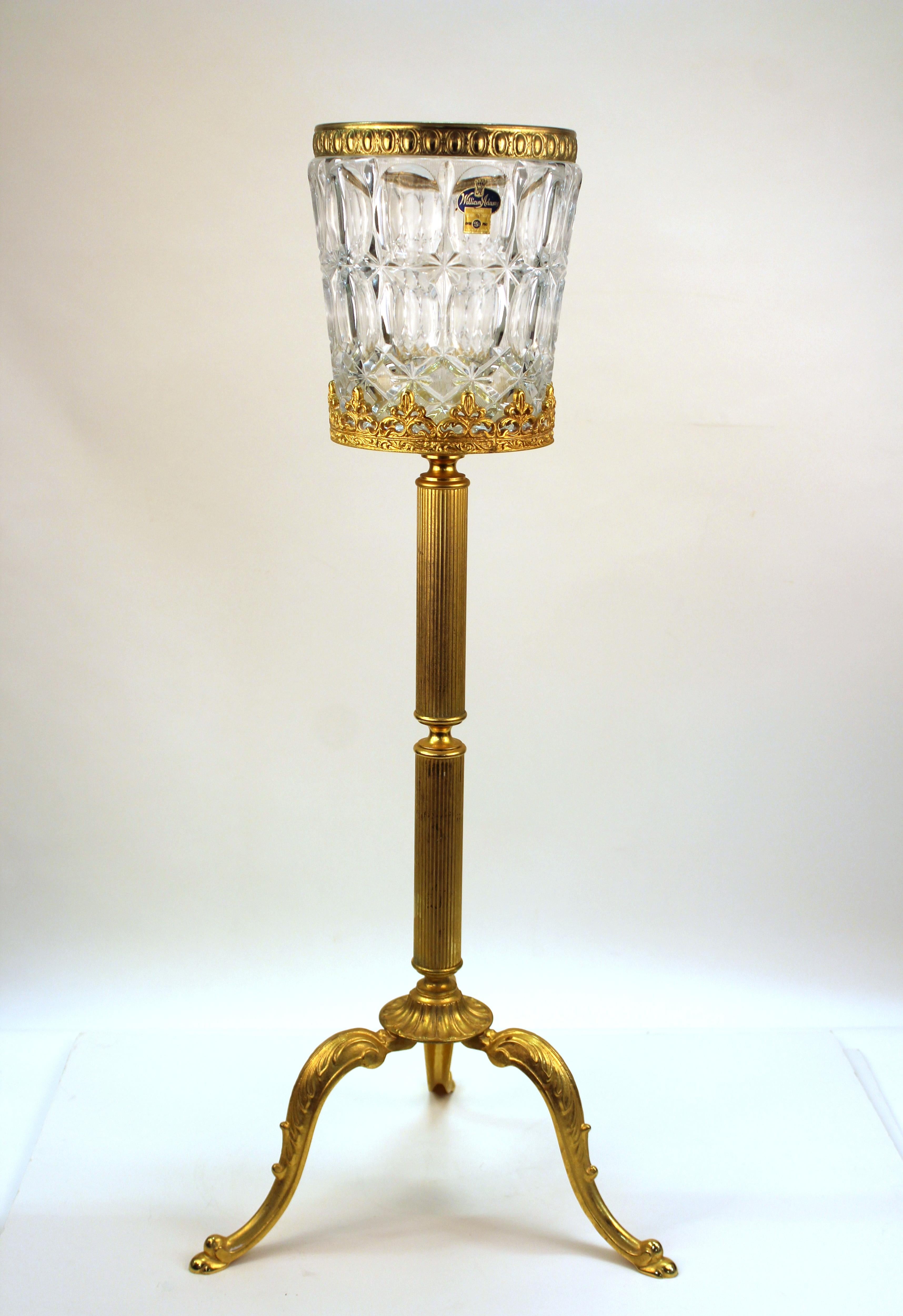 Champagne bucket from Germany produced during the mid-20th century. Features include a clear cut crystal bucket with geometric faceted designs and a 24-karat gilded stand. The piece stands on three curved legs and an intricate column body. A German