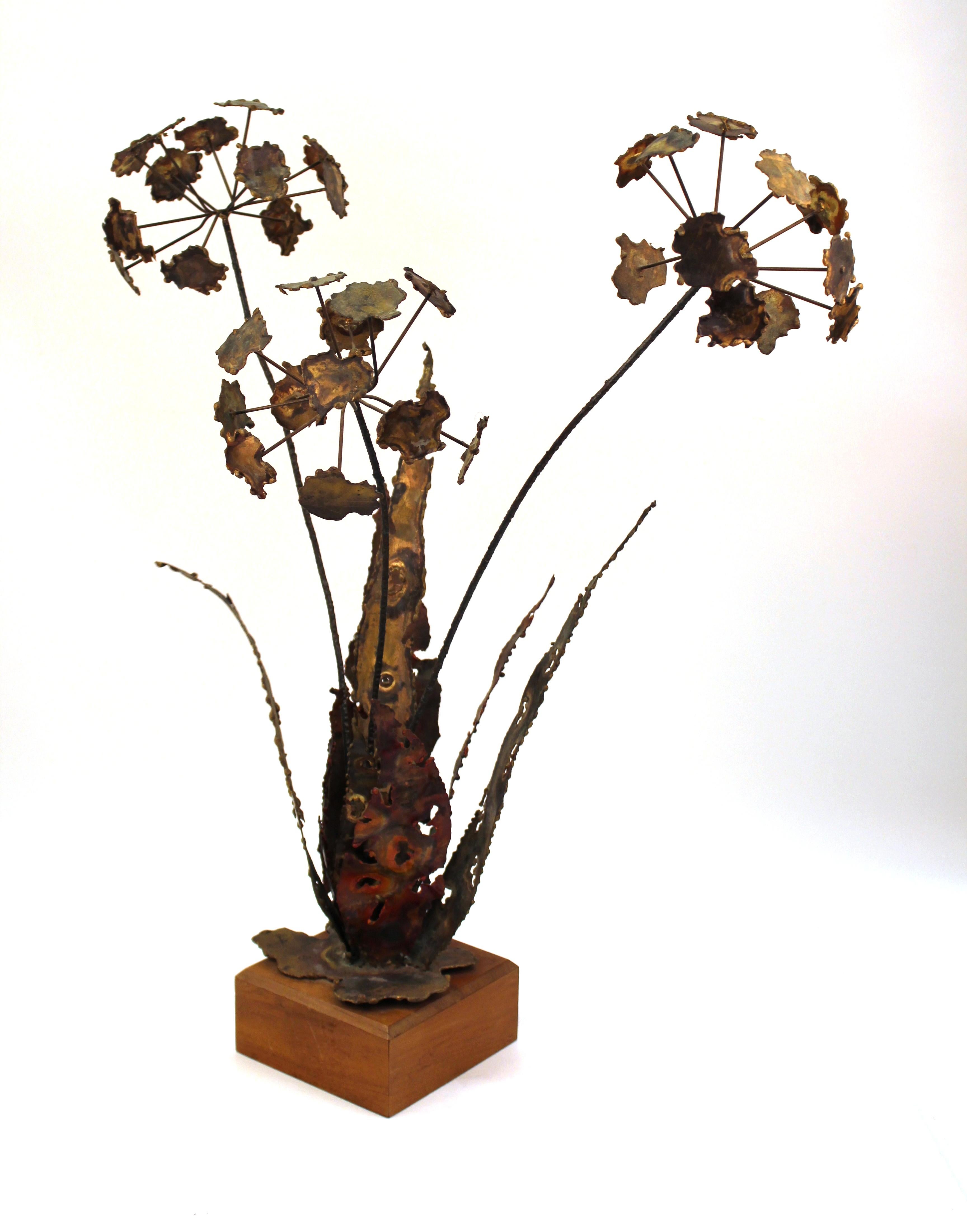 Silas Seandel Brutalist sculpture of a spray of flowers in distressed patinated metal. Features in include three long steams with a bushel of flowers at the top of each. The flowers are surrounded by several long pointed leaves and are supported by