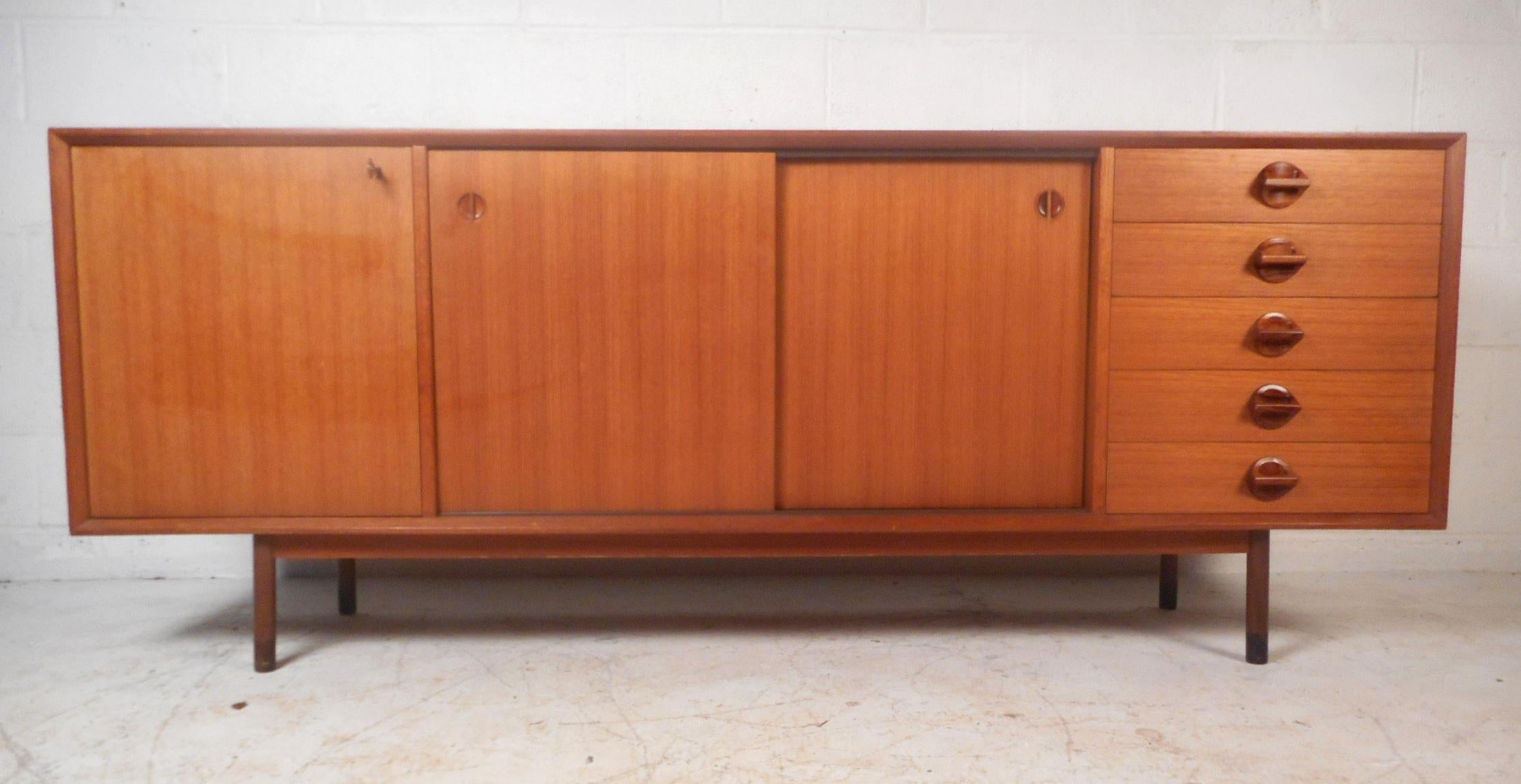 A stunning Mid-Century Modern sideboard with sculpted rosewood pulls, a finished back, and a rich vintage teak finish. Stylish Italian design with ample storage space within its large compartments with shelves hidden behind sliding doors. This