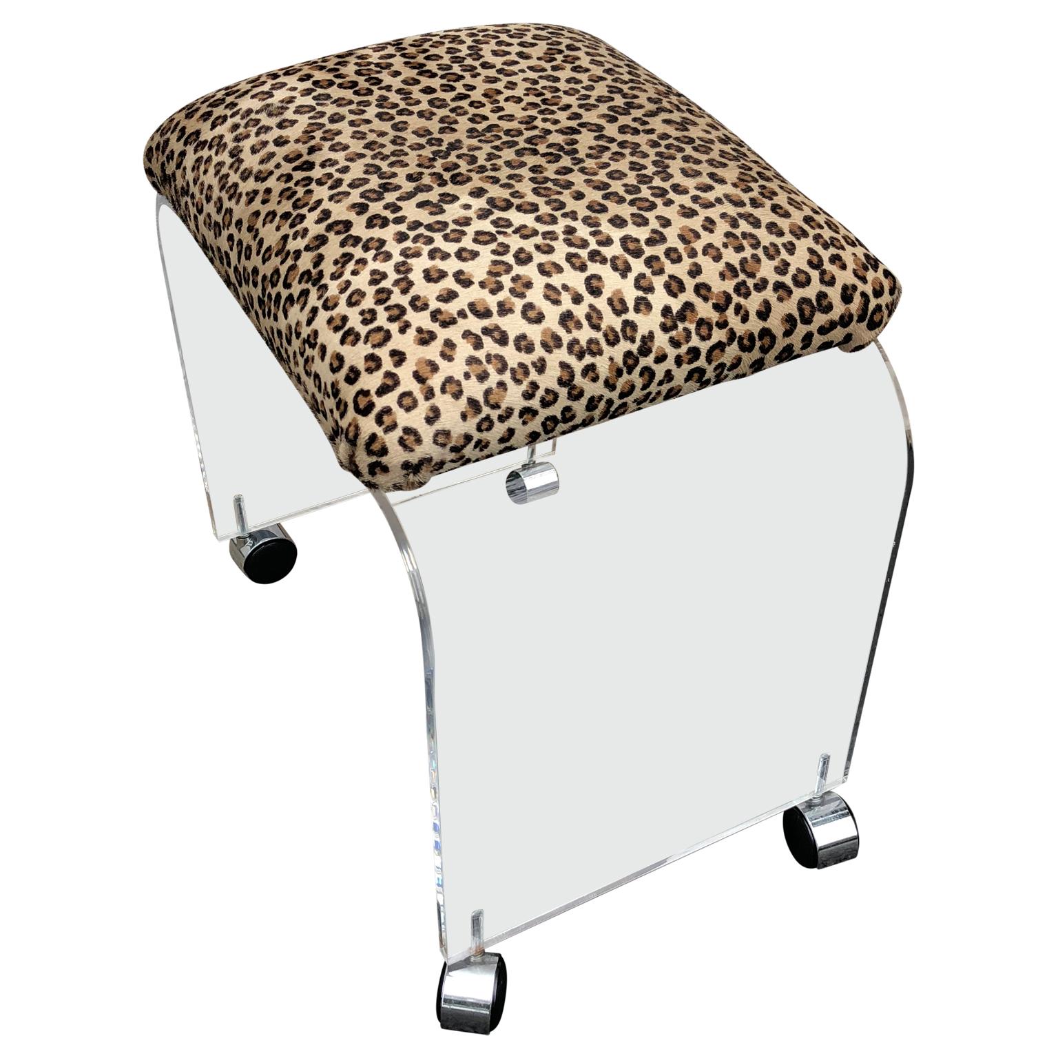 This bench or stool features a thick Lucite design with a waterfall design newly upholstered in faux cheetah fabric. It rests on castors which would make it well suited as a vanity stool. This stool is newly upholstered and on wheels.