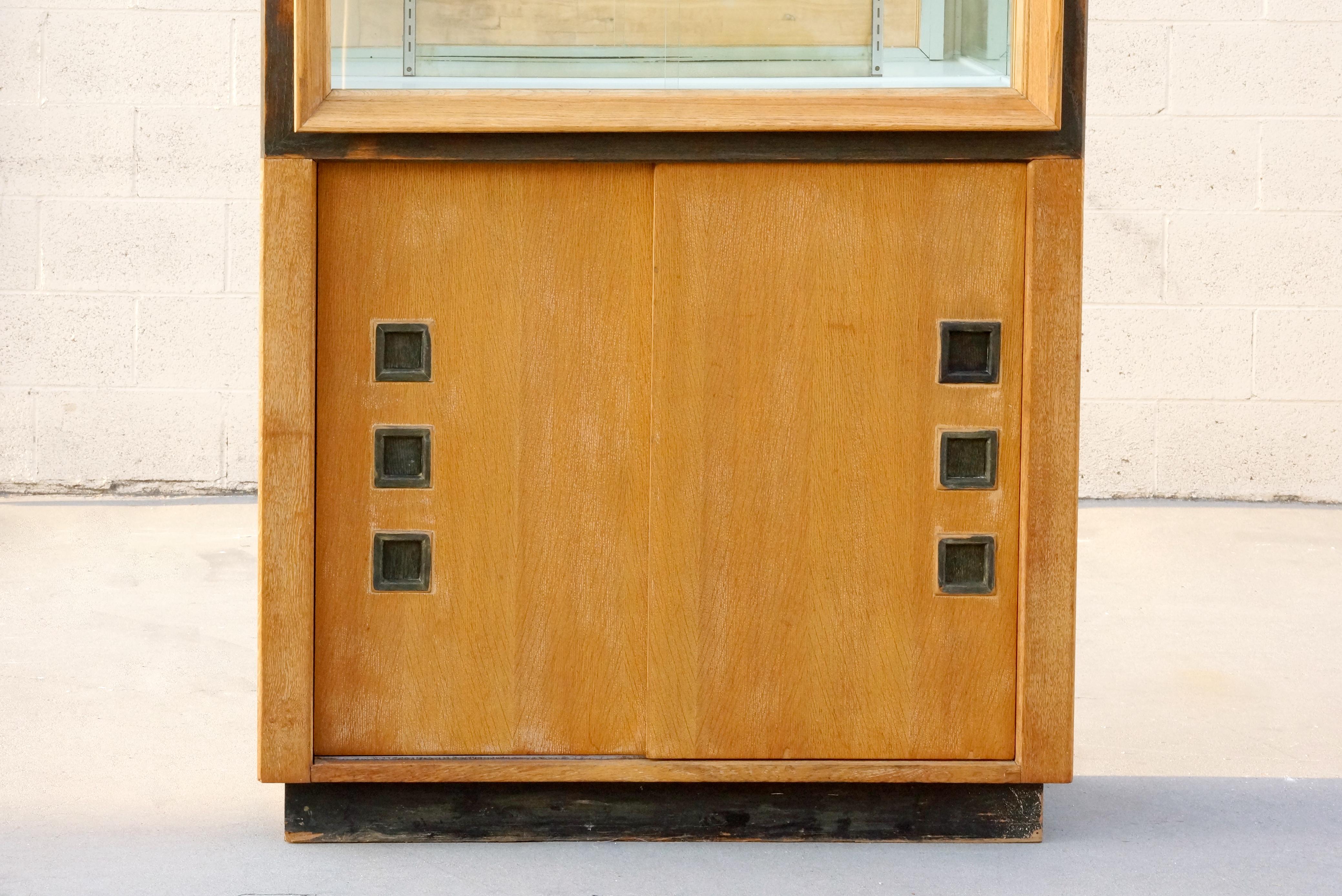 A most unique modernist display cabinet, unattributed but in the style of Paul Laszlo, circa 1940s. Composed of solid oak with sliding glass doors, adjustable glass shelves and mirror back on the top and sliding wood doors with wonderful inverted