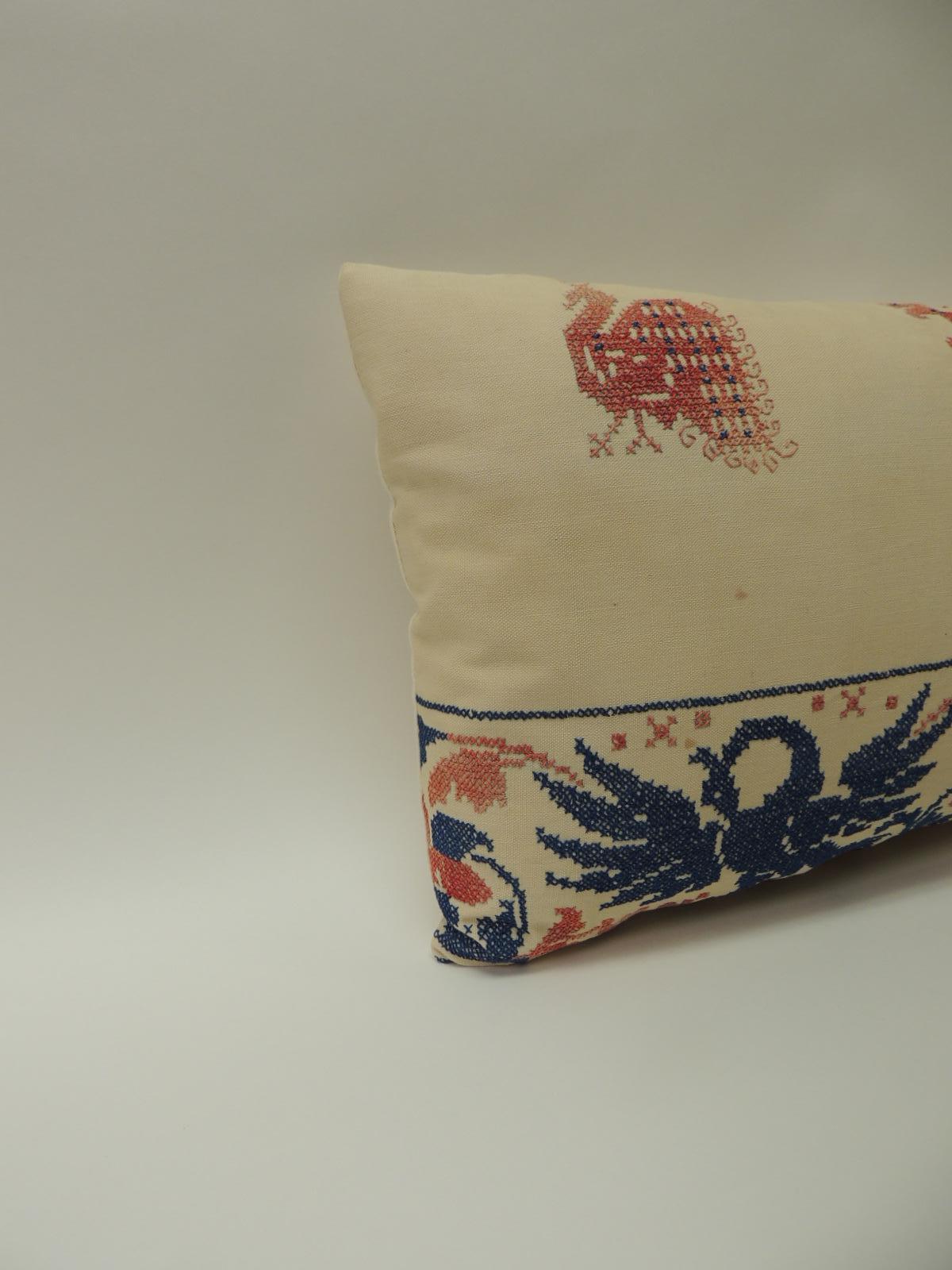 Red, blue and natural Greek Isle embroidered bolster’ pillow depicting embroidered birds and flowers (cross stitched) pattern; Decorative pillow finished in linen backing. Antique textile panel in shades of red, blue and natural. Decorative pillows