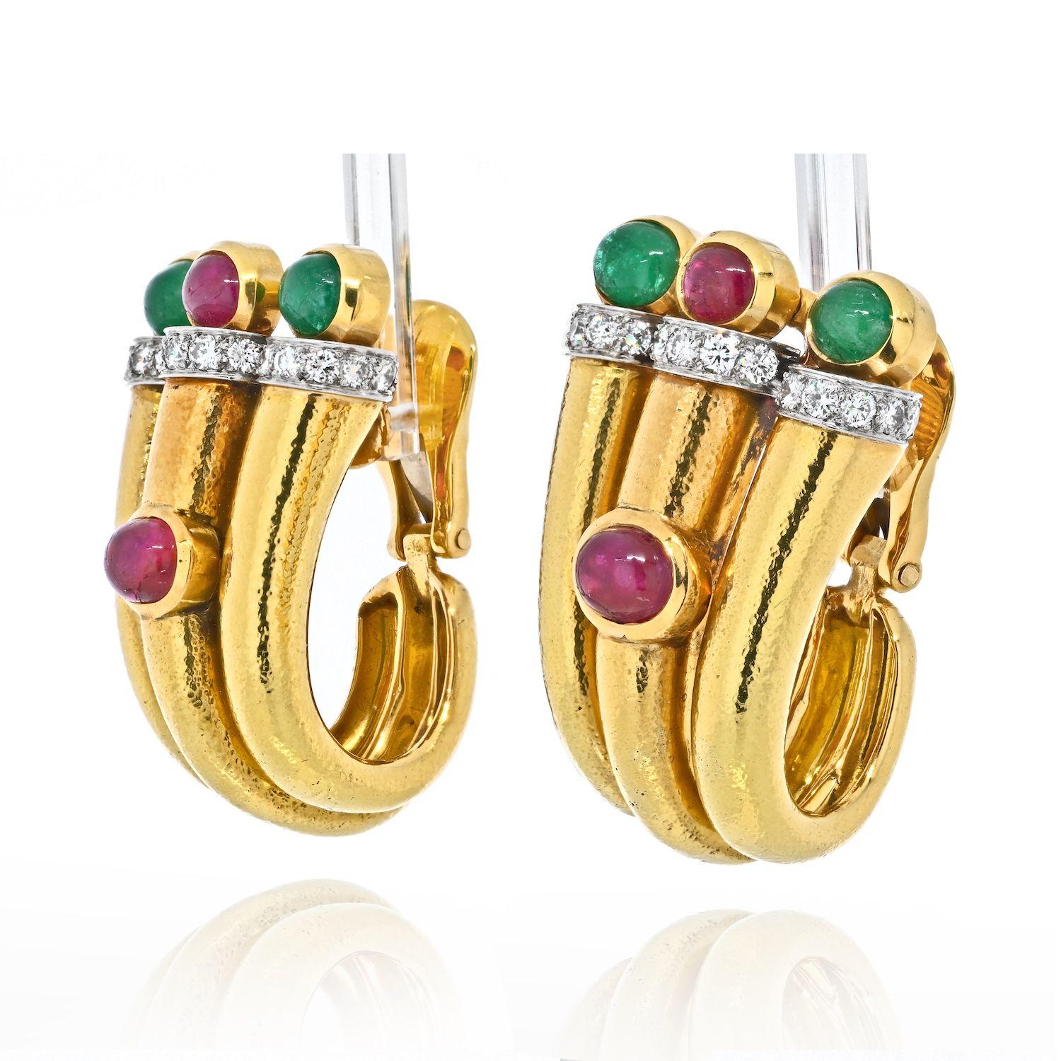 A stunning and rich look, these bold statement earrings by David Webb are of hand hammered 18K gold set with simply framed cabochon rubies and emeralds, then highlighted with diamonds, in a flattering shape that wraps under the earlobe. Clip and