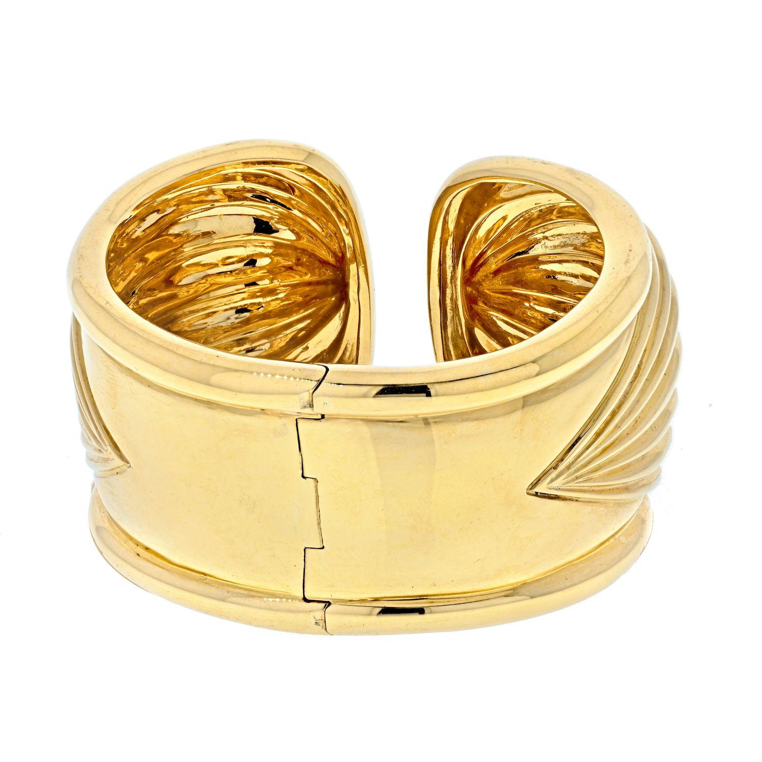 This very imposing fluted, 18k gold cuff bracelet by David Webb measures a full 1.7 inch wide at it's front, tapering down to 1 inches at the rear. 

The bracelet weighs over 100 grams in 18k gold creating a striking appearance. Hinged in the back