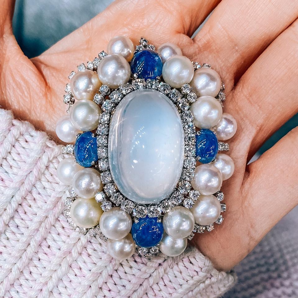 This vintage platinum brooch is a true masterpiece created by the renowned American jewelry designer, David Webb, in the 1960s. The brooch features an exquisite oval cabochon cut moonstone at its center, which is surrounded by a stunning halo of