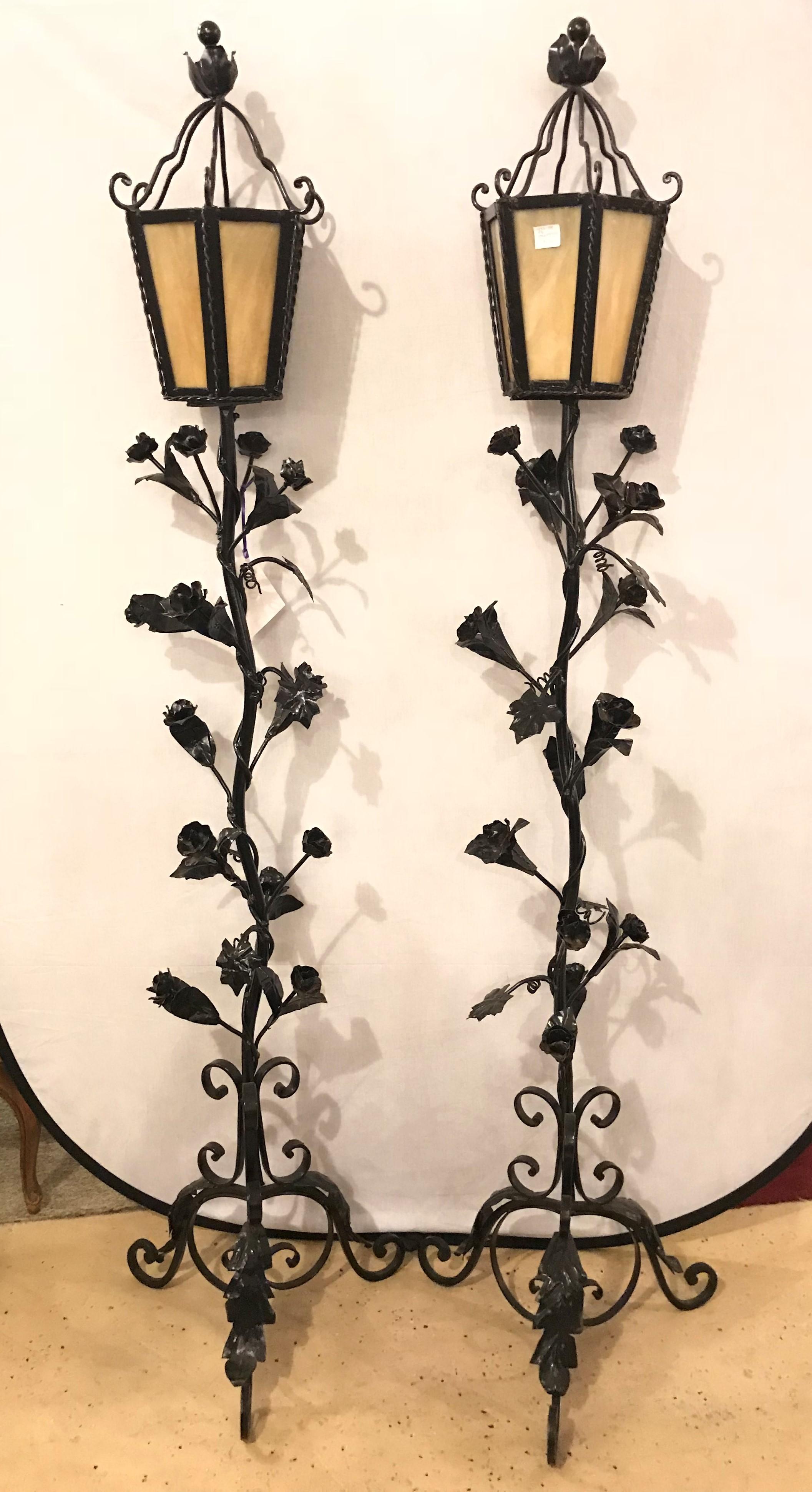 A pair of black late 19th or early 20th century painted art glass lidded torchieres with leaves and roses. These fine iron standing lanterns each have a wonderfully decorative ebony frame with flowing leaf, vine and rosettes on the stem leading to