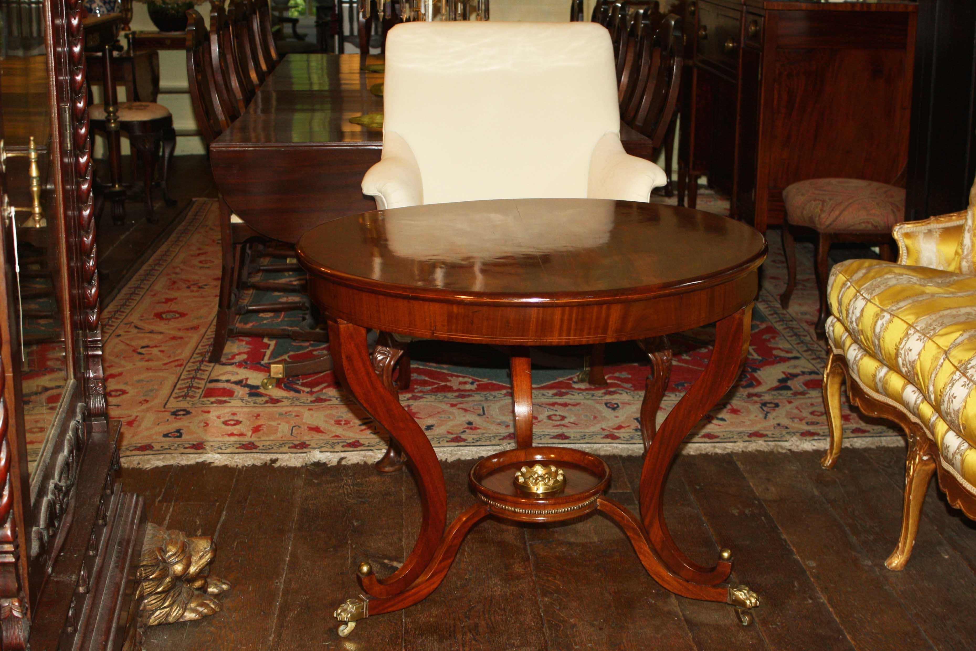 German round center table to the neoclassical taste. Mahogany with boxwood string inlays. Brass details include a floral circular mount in the dish stretcher platform, row of brass beading, and ball mounted paw form casters. Related examples: see