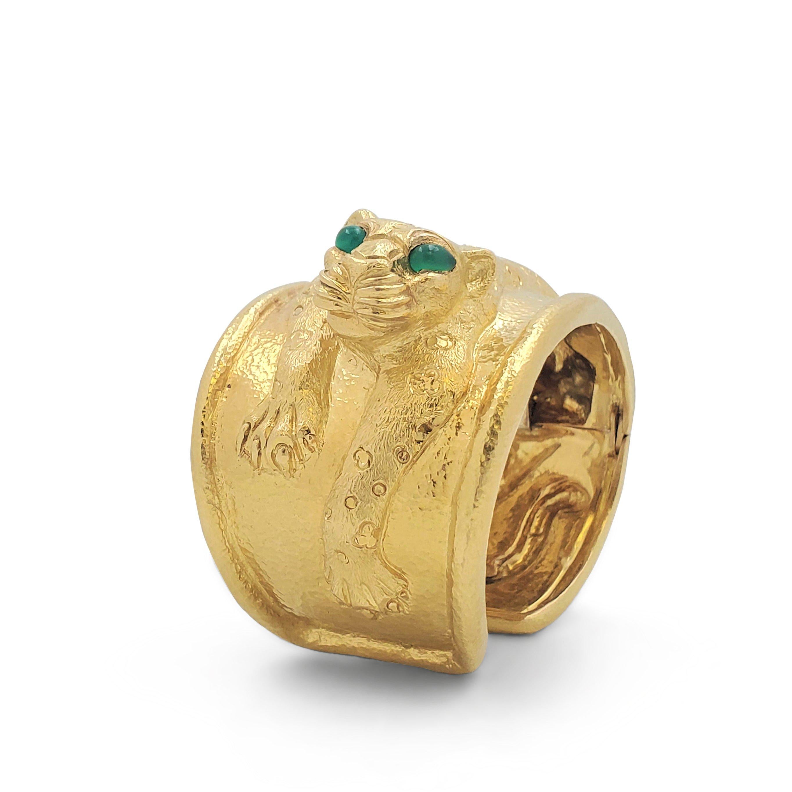 Authentic David Webb 'Repoussé Leopard' cuff bangle crafted in 18 karat yellow gold with enchanting emerald eyes. Designed as a sculptural Leopard in hunting posture, ready to pounce.  The leopard's coat is delicately engraved in a flower pattern,
