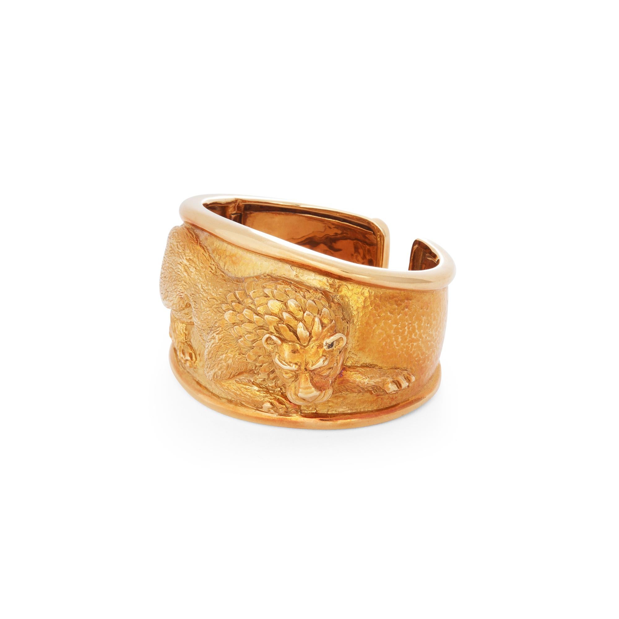 Authentic David Webb Repoussé Lion cuff bracelet crafted in 18 karat yellow gold.  Designed as a sculptural lion in hunting posture, ready to pounce.  The lion's coat and mane are delicately engraved to resemble a lion's fur and the hammered texture