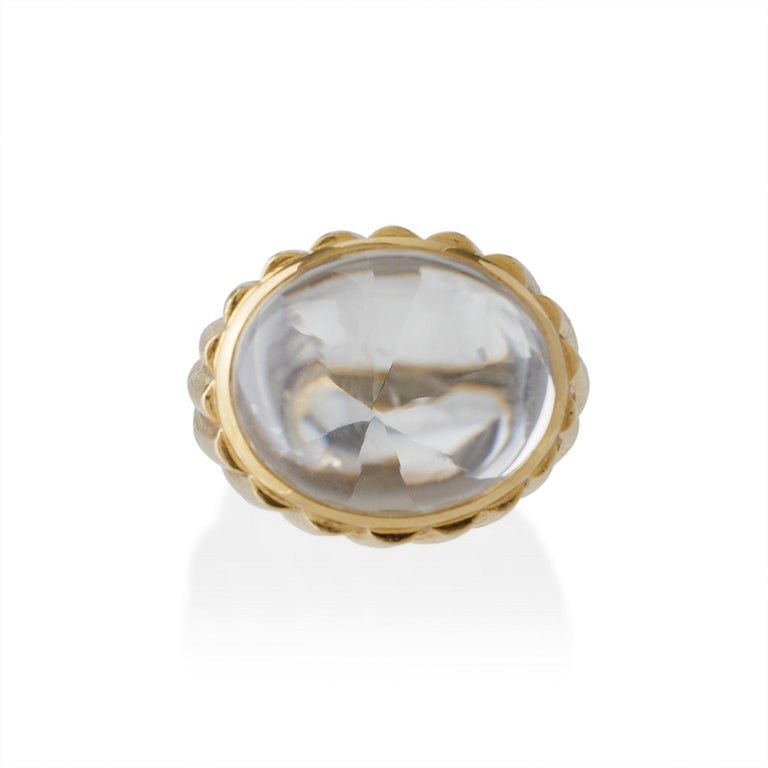 Dating from the 1960s-1970s, this hammered 18K gold and rock crystal bombé ring was created by David Webb, New York. The ring is set with a high domed rock crystal cabochon with a faceted pavilion above a hammered gold mount with an obliquely ribbed