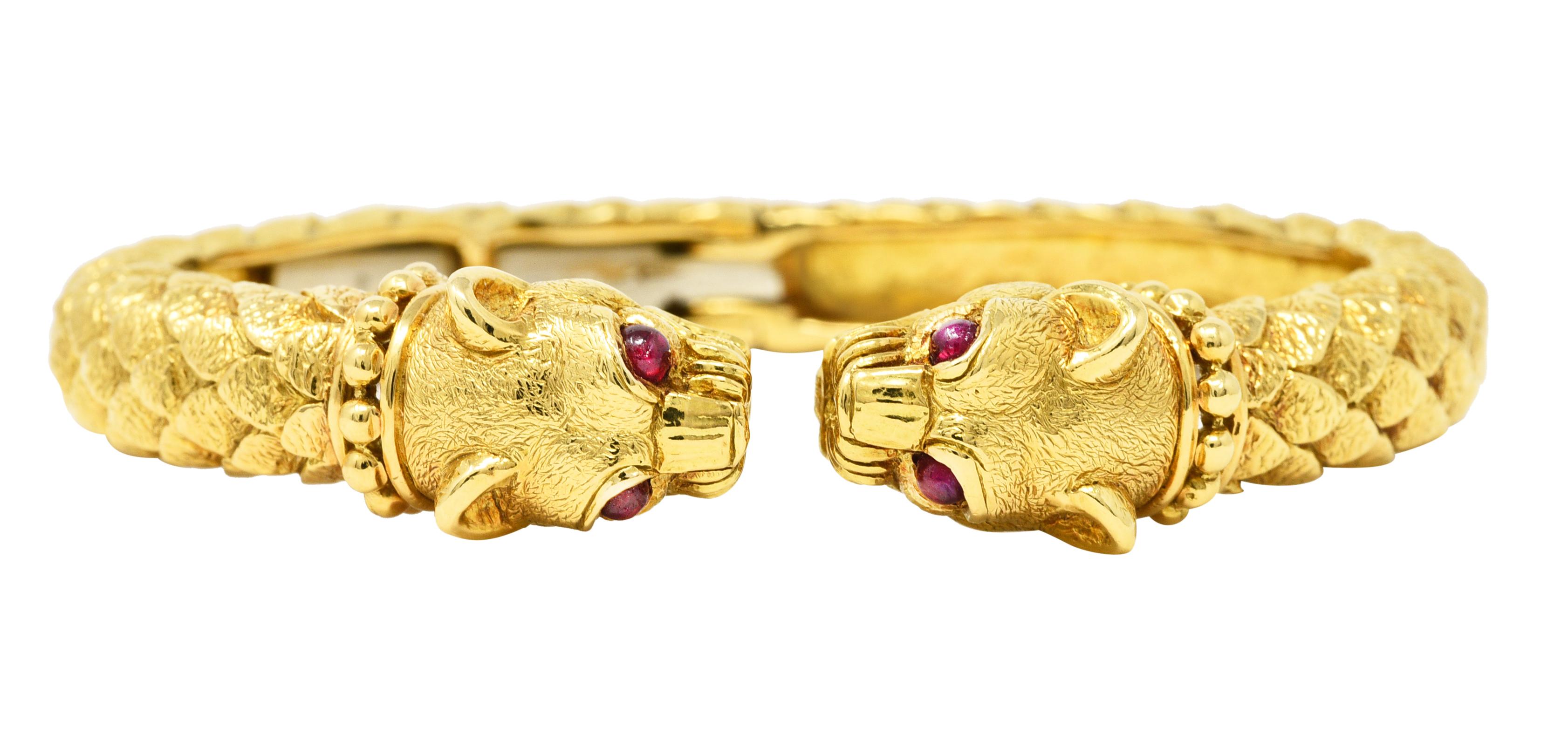 Cuff bracelet designed as two stylized panther heads with texturous scales. Featuring gold bead collars, detailed snarling faces, and textured fur. Each panther head has two 2.5 mm round ruby cabochon eyes. Rubies are well matched medium red in