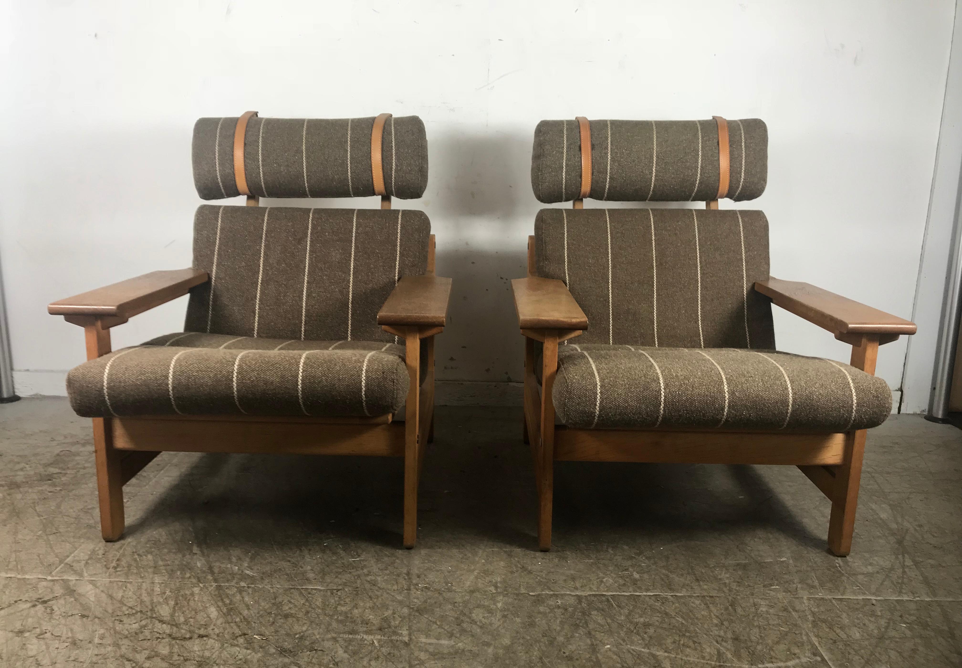 Stunning pair of paddle arm lounge chairs by Aksel Dahl, made in Denmark, superior quality and construction,Solid oak frames with a wonderful warm patina, retain they are original wool striped upholstery as well as leather straps, in excellent