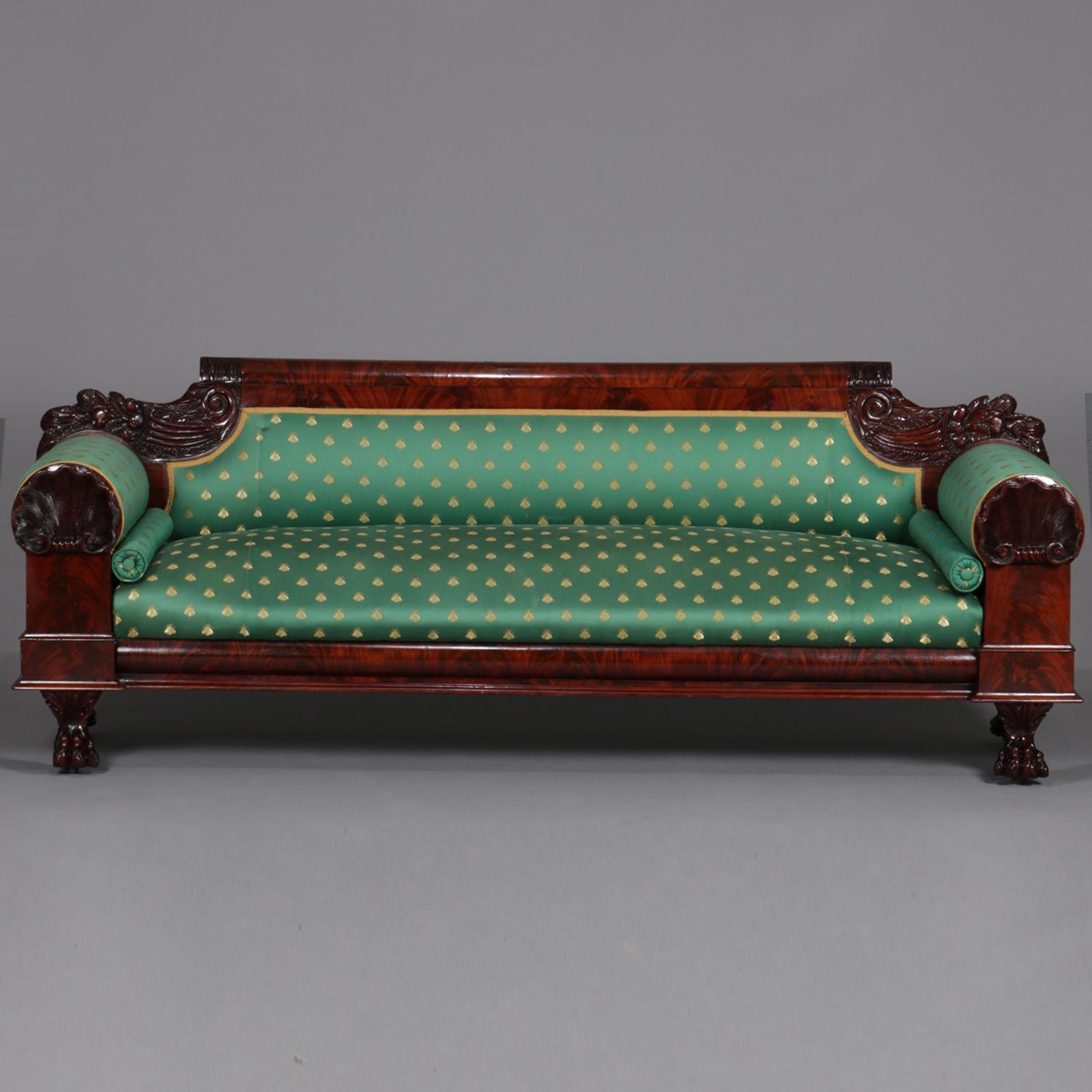 Classical American Empire sofa features flame mahogany frame with deeply striated back rail flanked by carved cornucopia, oversized rolled arms with carved shell surmounting column-form supports raised on lion paw feet and with deeply striated ogee