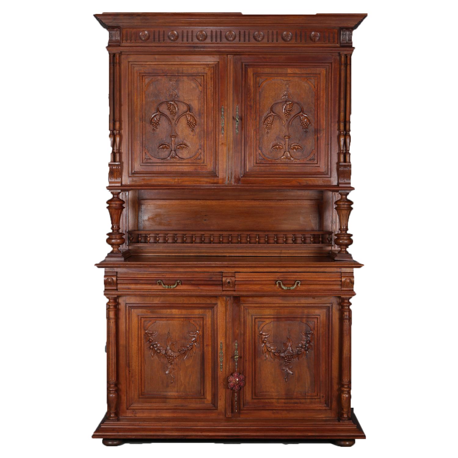Antique English court cupboard features oak construction with upper having two panelled doors with carved corbels framing vineyard grape leaf and vine reserves opening to shelved interior supported by stepped and turned columns over lower case