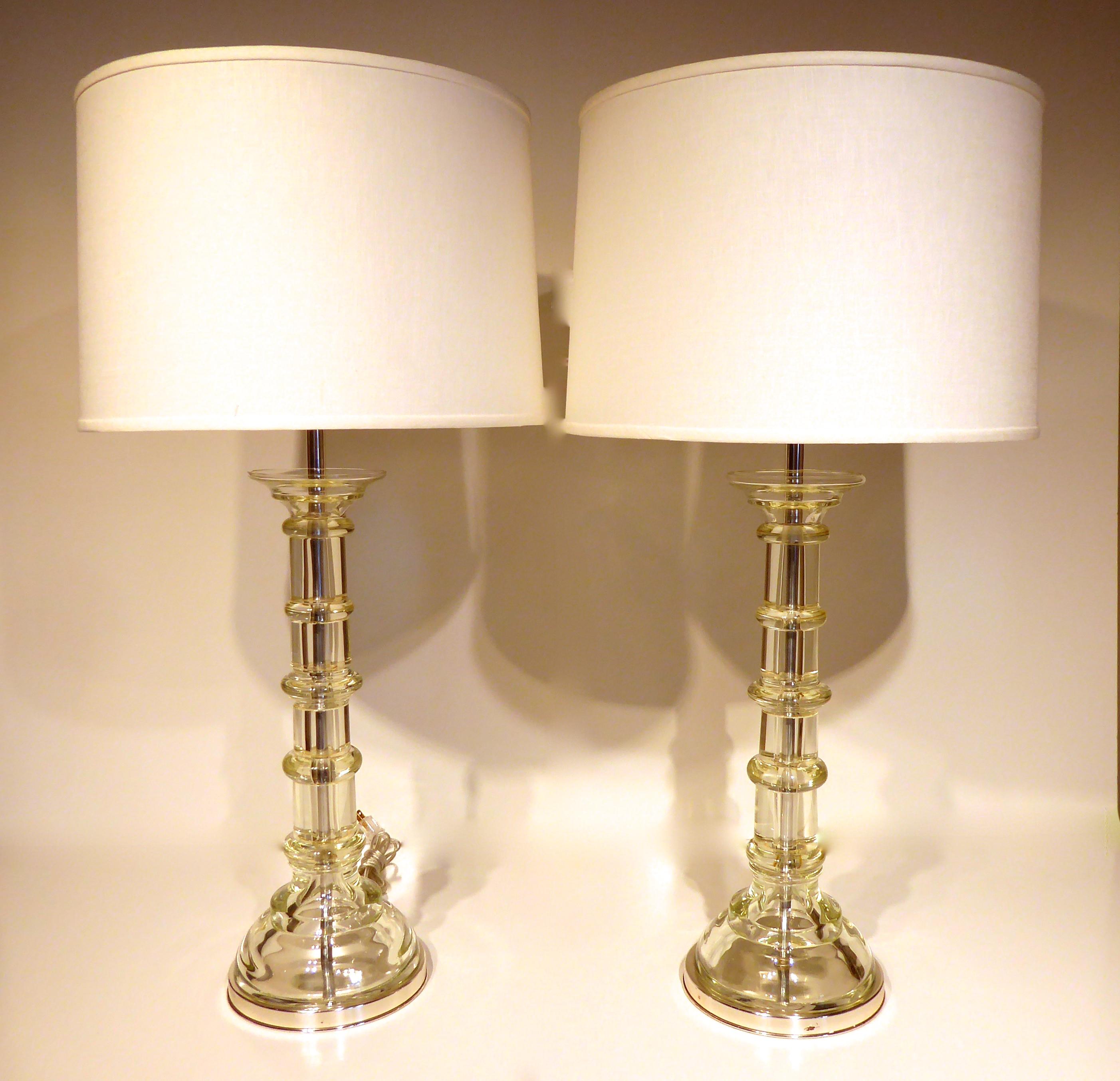 A pair of clear Murano glass column-form table lamps made by The Marbro Lamp Company, circa 1960s. The lamps sit on chrome-plated metal bases and retain all of the original metal fittings and finials. They also retain the Marbro label. The