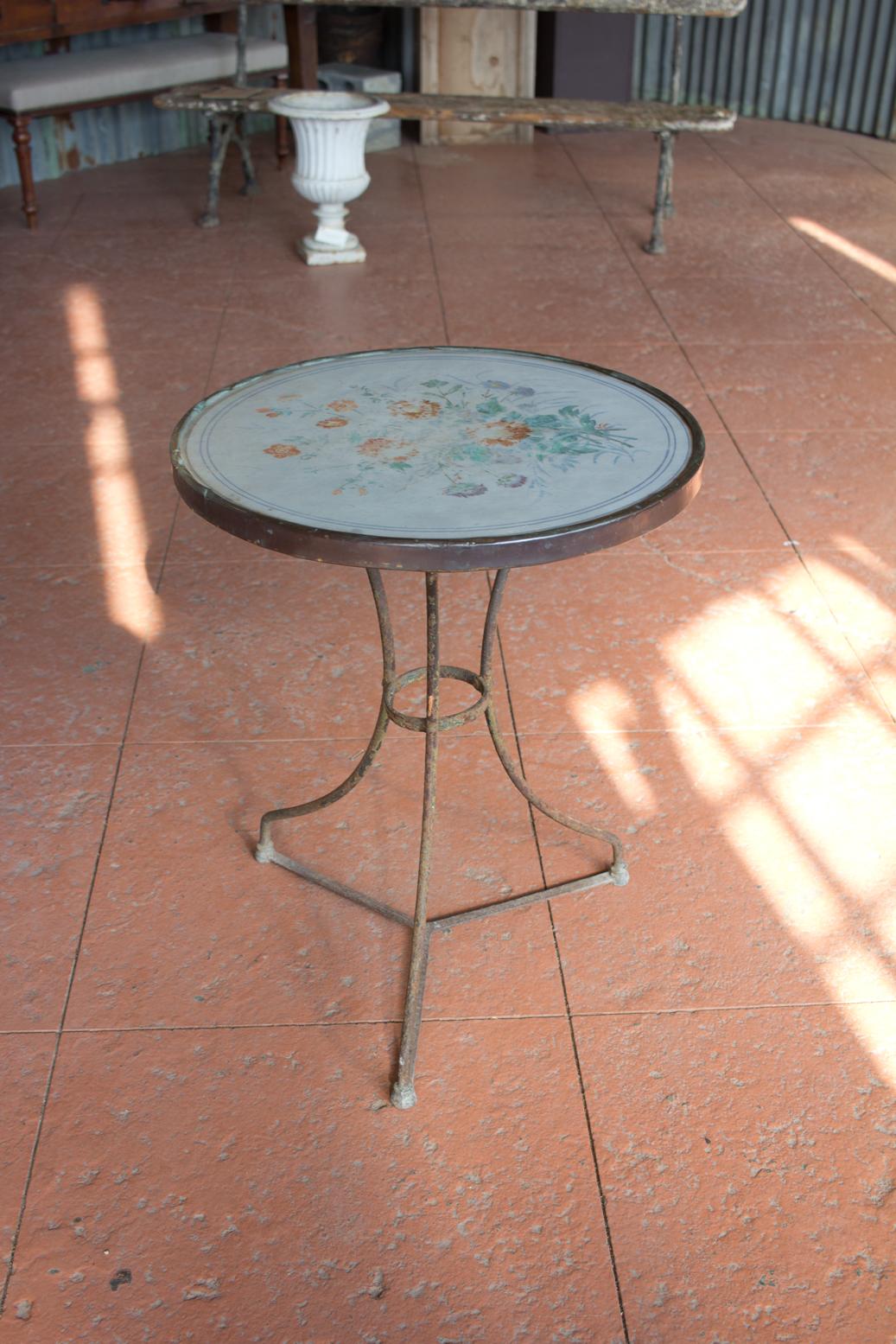 Unusual antique French bistro table with a hand-painted ceramic top that is beautifully faded with age. The top is set in a copper band, on a wrought iron tripod base.