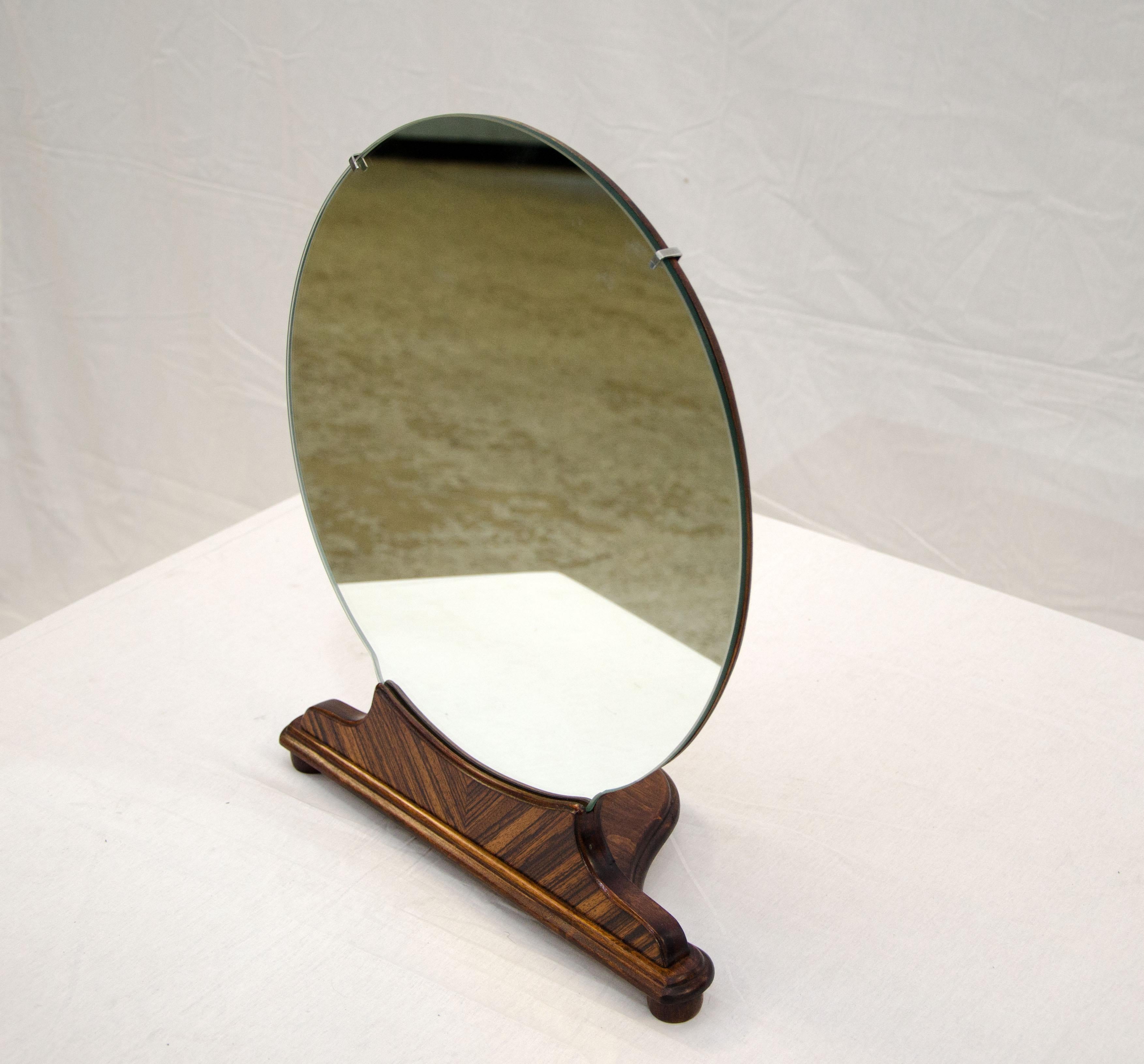 This small walnut freestanding mirror was made to be used on top of an Art Deco high-boy dresser. It is supported by three ball feet on a wooden framework and has a book-matched walnut decorative grain pattern on the front. The mirror itself is 15